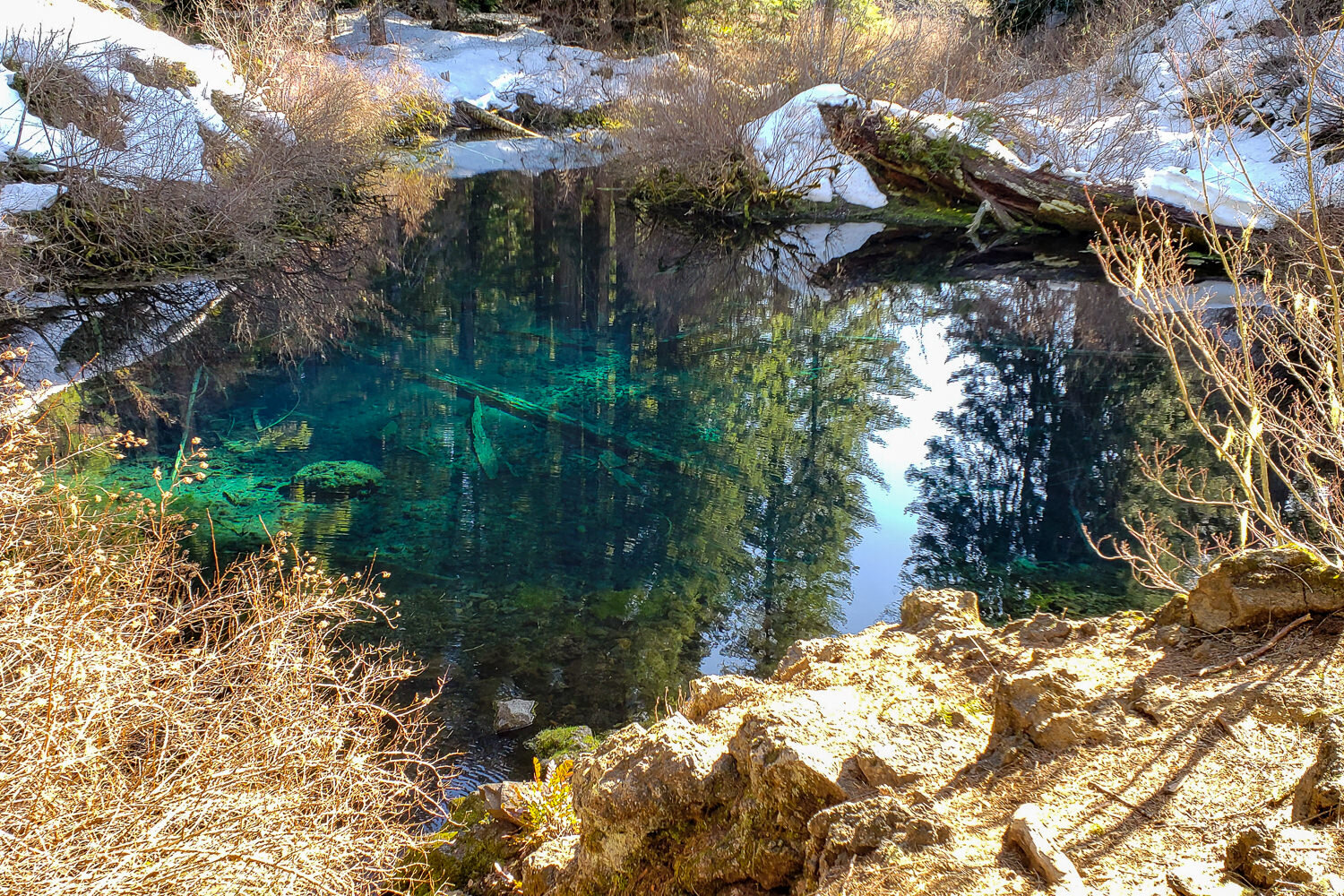 a bright blue-green spring surrounded in snow and sunny rocks. The source of the Mckenzie river