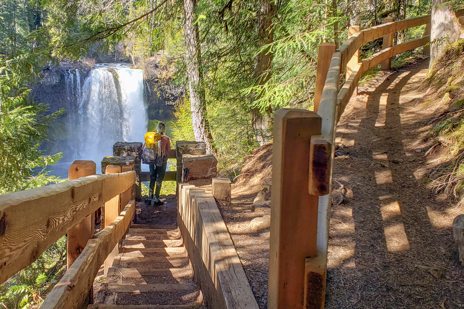 backpacker walking down some wooden steps to a large waterfall in oregon