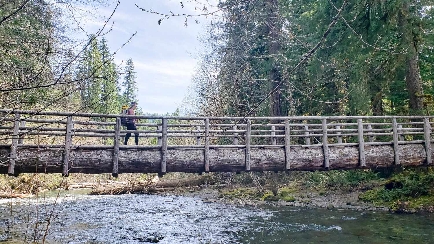 backpacker crosses a wooden bridge over the mckenzie river in oregon