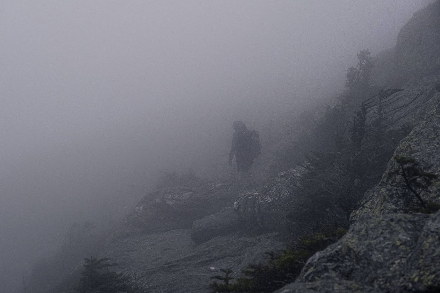 backpacker on the long trail walking on a rocky slope in dense fog.