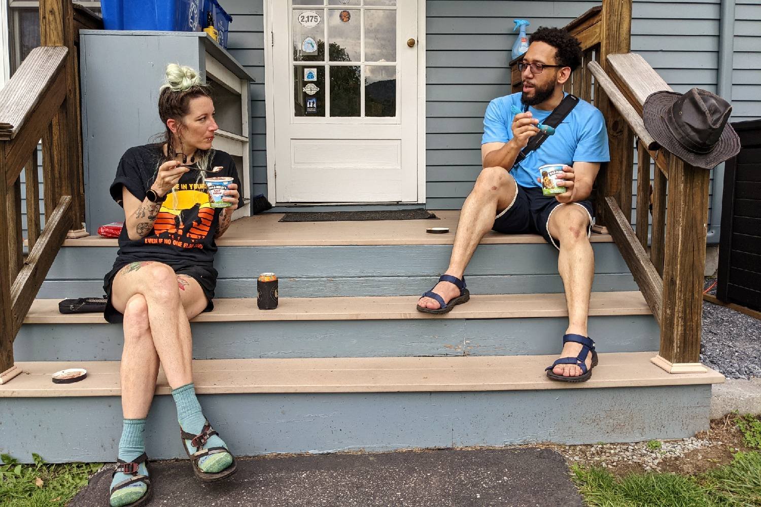 two long trail hikers sitting on a stoop of a general store eating pints of ben and jerry's ice cream.