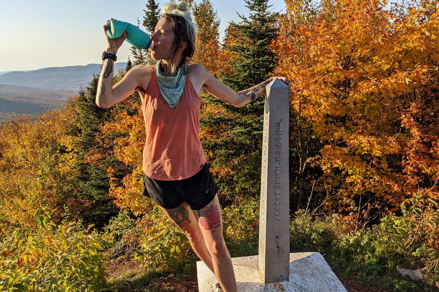 backpacker posing next to the northern terminus monument in the fall on the long trail with clear skies and fall foliage. 