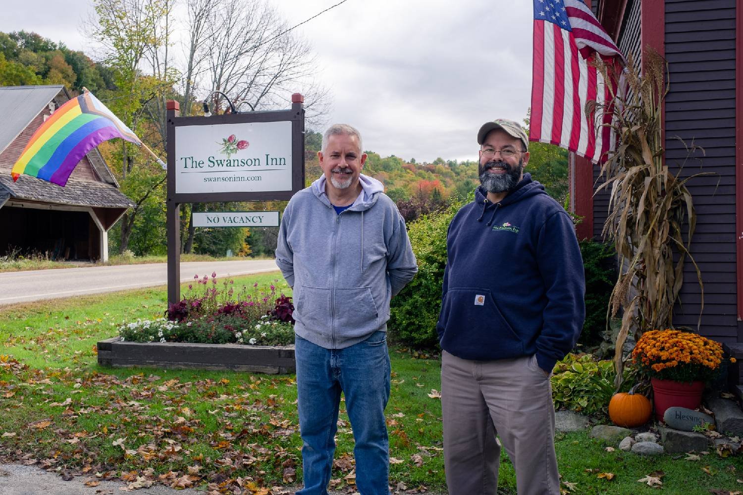 two owners posing in front of the Swanson Inn with the building sign and an LGBTQA+ and American flag in the background