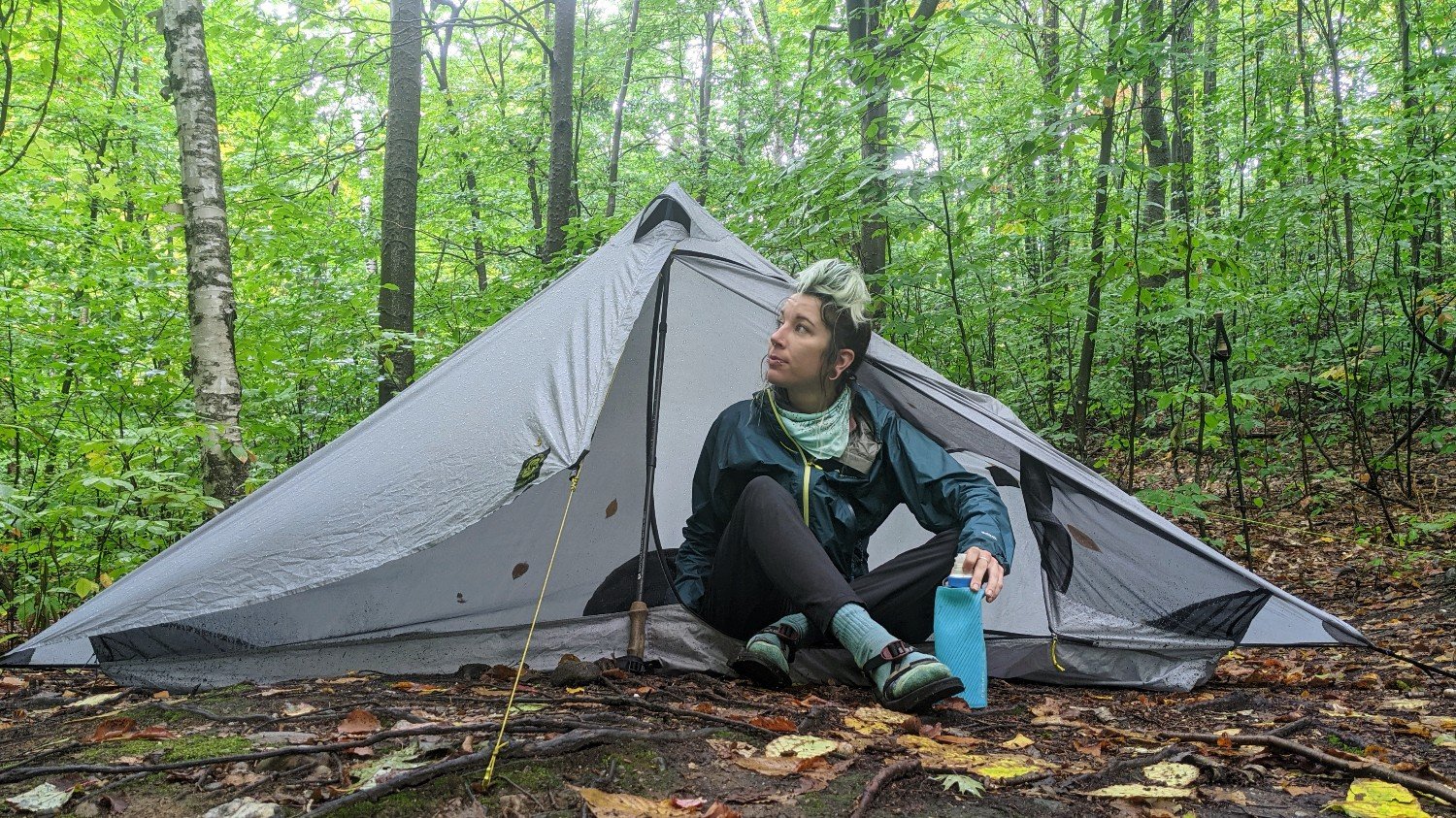 backpacker on the the long trail sitting at the door of her one person tent in a green forest.