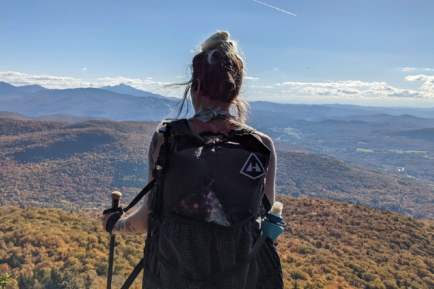 a long trail thru-hiker overlooking the fall foliage blanketing the mountains and hills below.