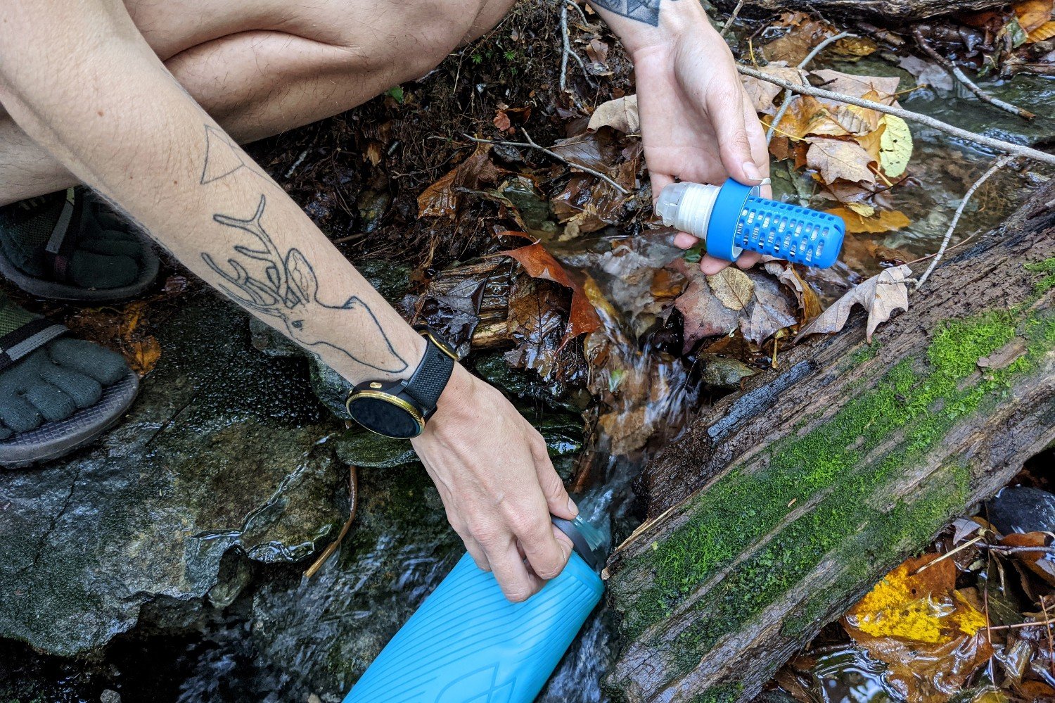 Backpacker's hands holding onto their water filter system as they refill their water bottle in a small stream on the long trail in Vermont.