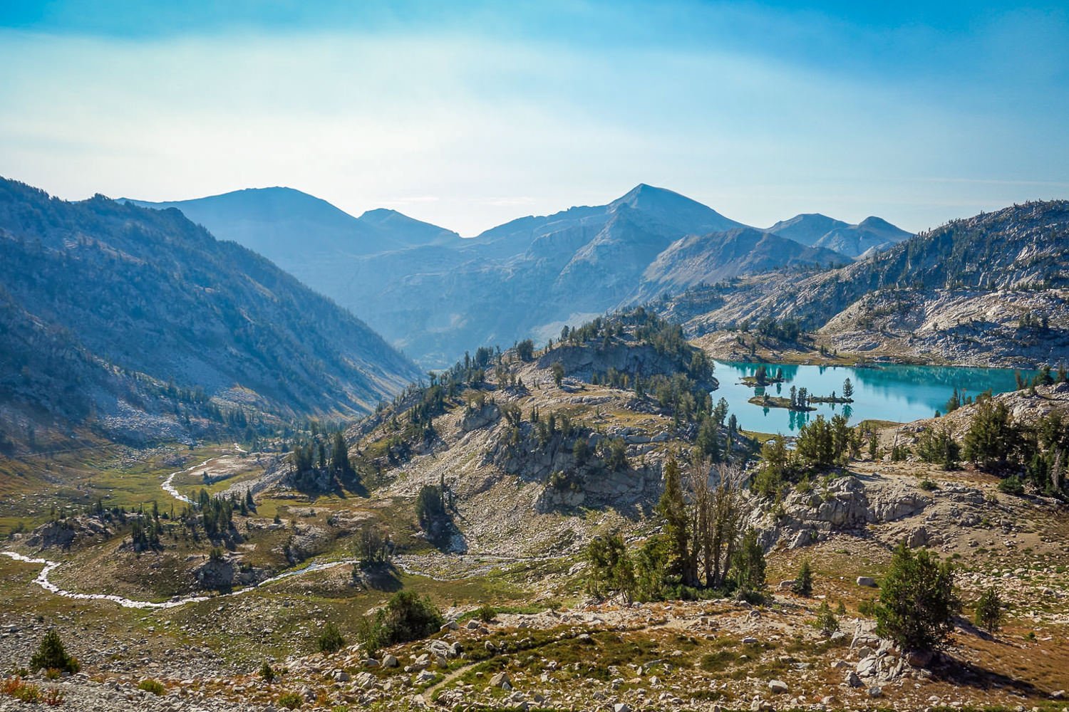 turquoise lake rests in a pocket of a mountain with a valley sloping below and peaks in the distance in the wallowas in oregon