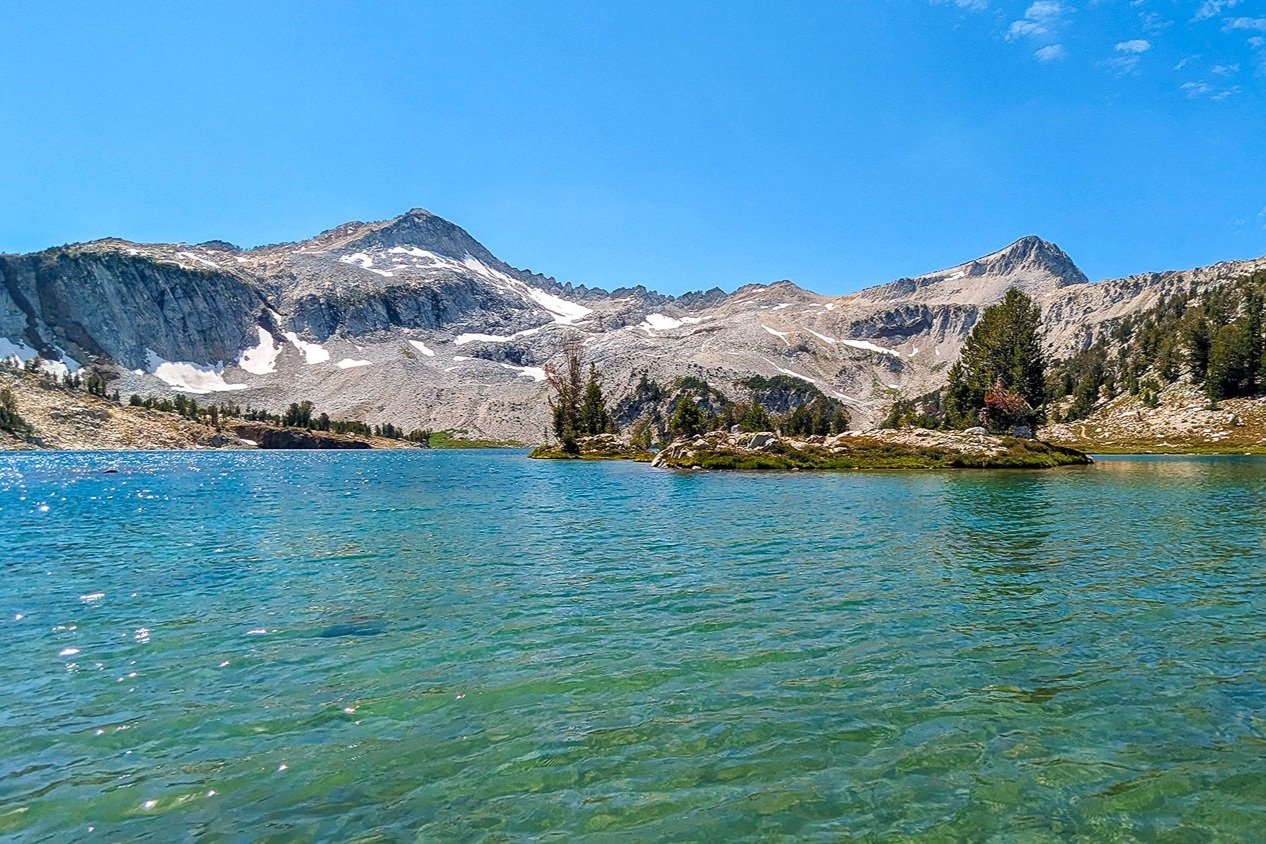 blue and turquoise clear water below a snow patched granite ridge in the eagle cap wilderness.