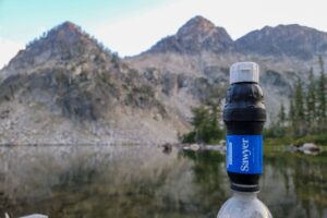 a water filter system attached to a water bottle with a still alpine lake and a mountain behind it.