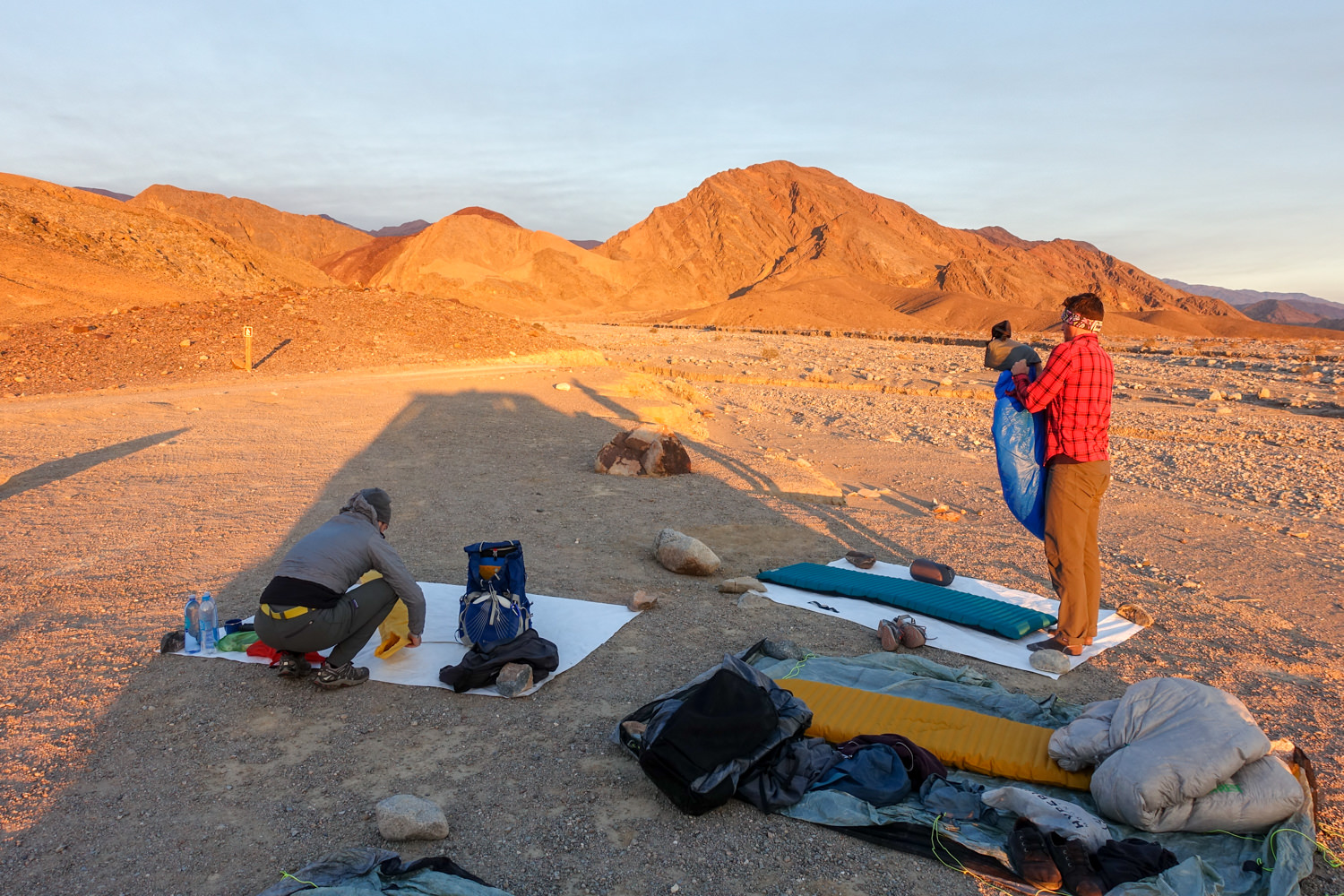 backpackers set up camp during golden hour with the mountains casting shadows over their campsite.