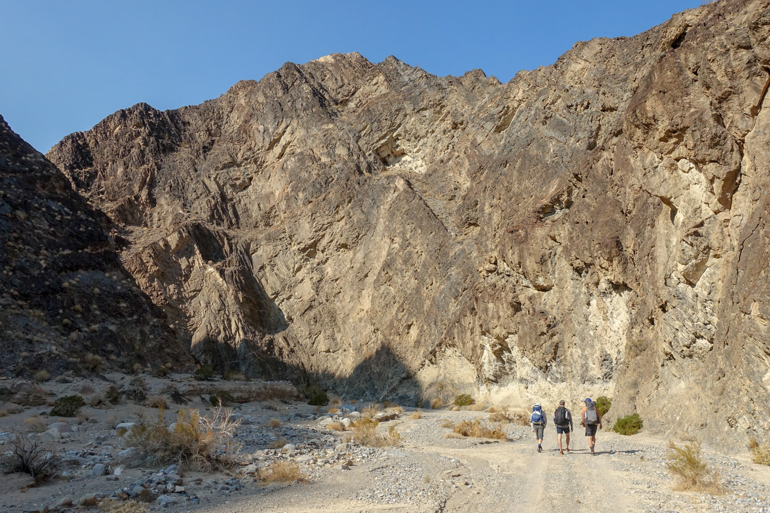 three backpackers in death valley walking toward the shade of a canyon