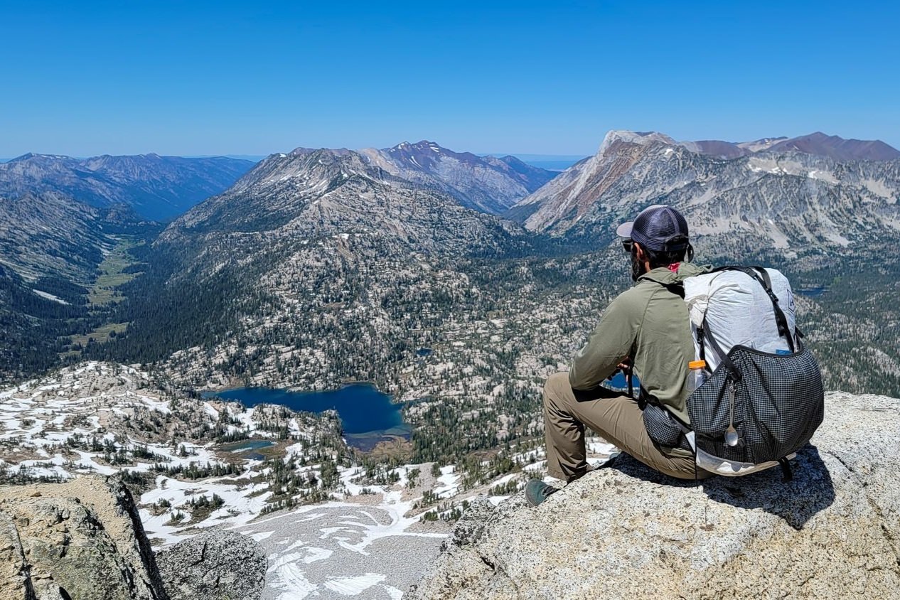 backpacker sitting on a large boulder looking out from the summit of eagle cap over lakes and valleys in the wallowa mountains.