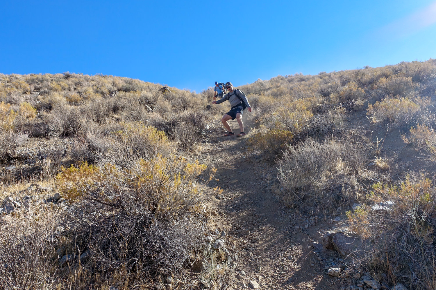 backpackers on the cottonwood marble canyon loop hiking down a steep loose trail with pokey brush around them