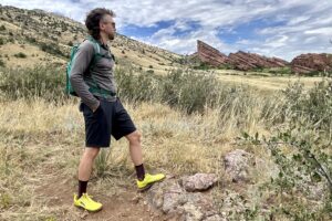 A hiker poses at an overlook with large red rocks in the background.