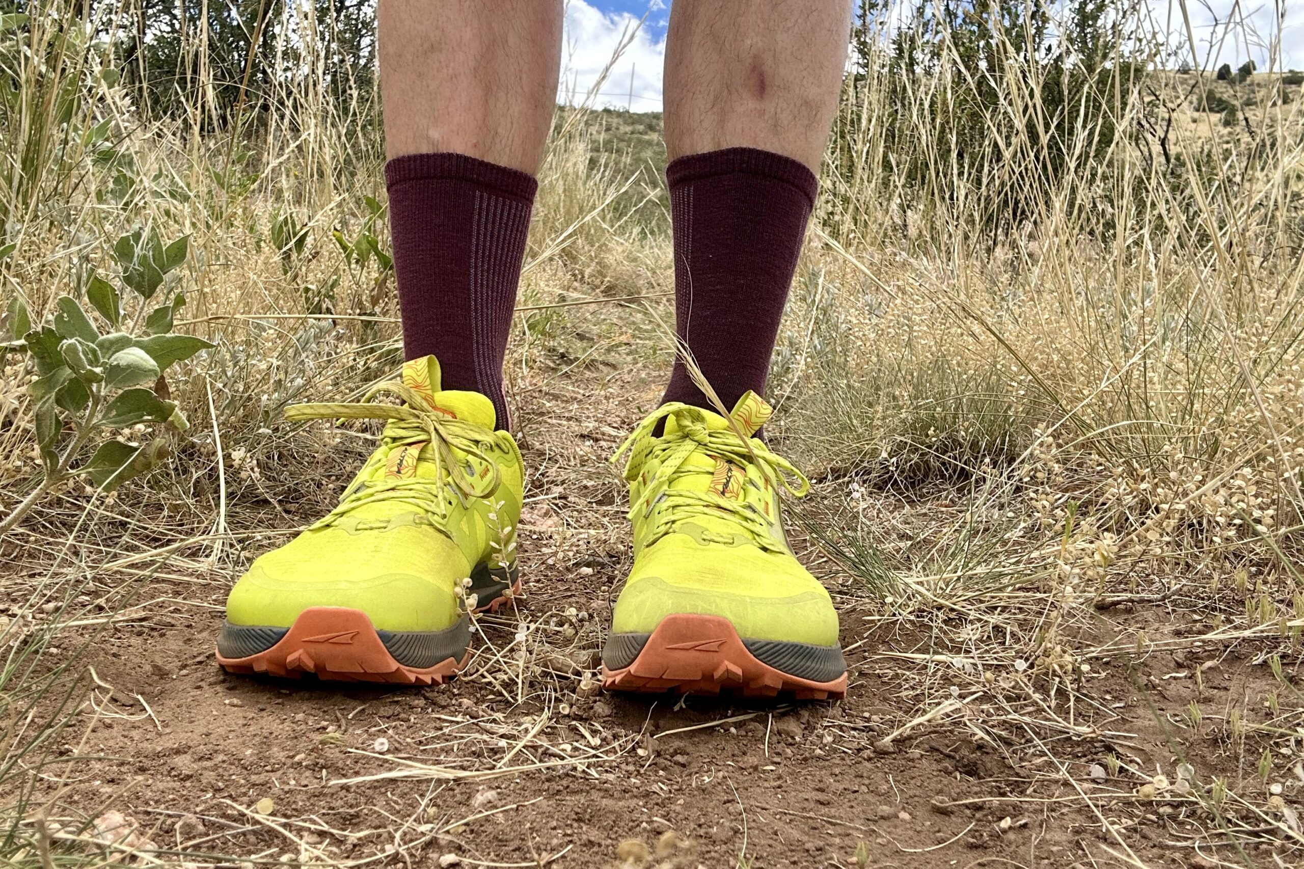 A close up, straight on shot of a hiker from the ankles down wearing trail runners in a desert setting.