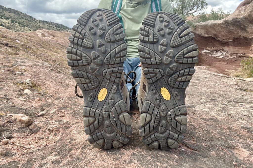 A hiker sits with their feet outstretched to the camera showing off the lugs and grip pattern of the Merrell Moab 3s.