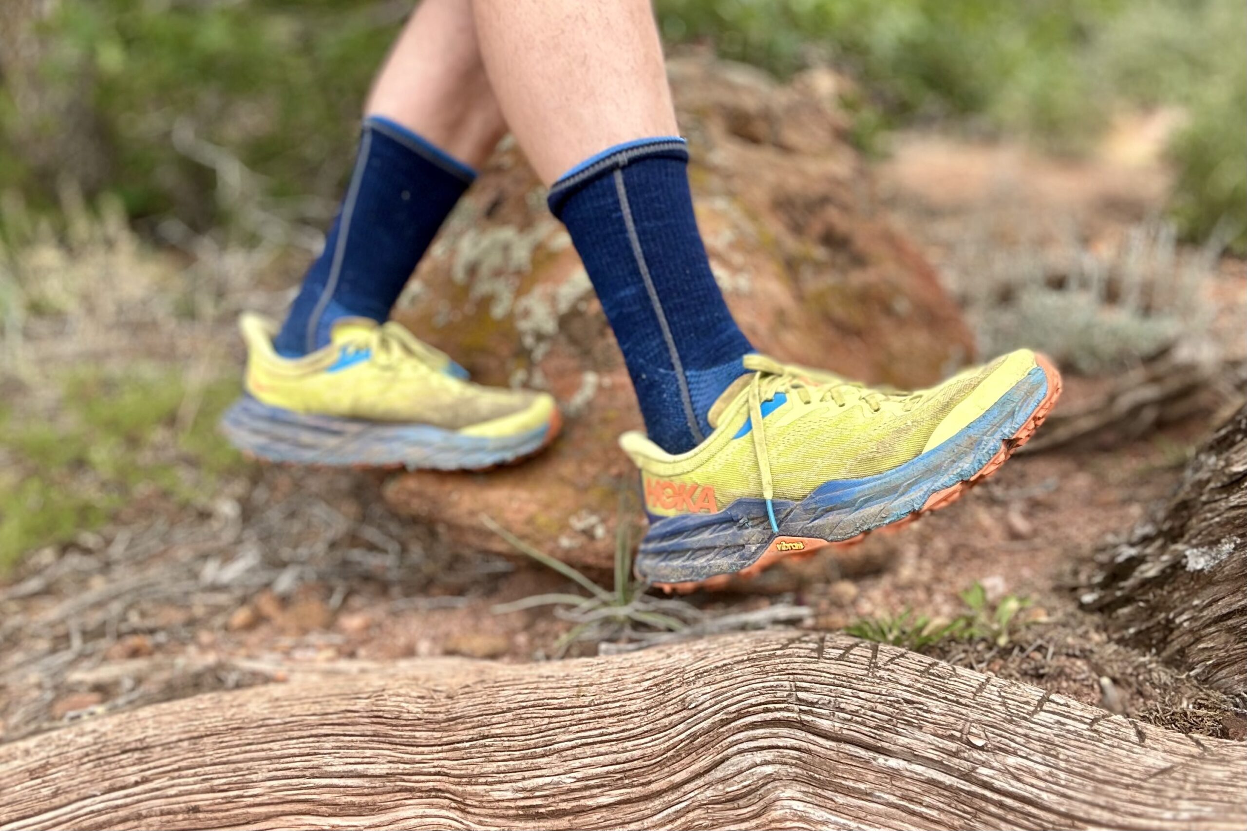 Closeup of trail running shoes from the knees down in a desert setting from a side profile.