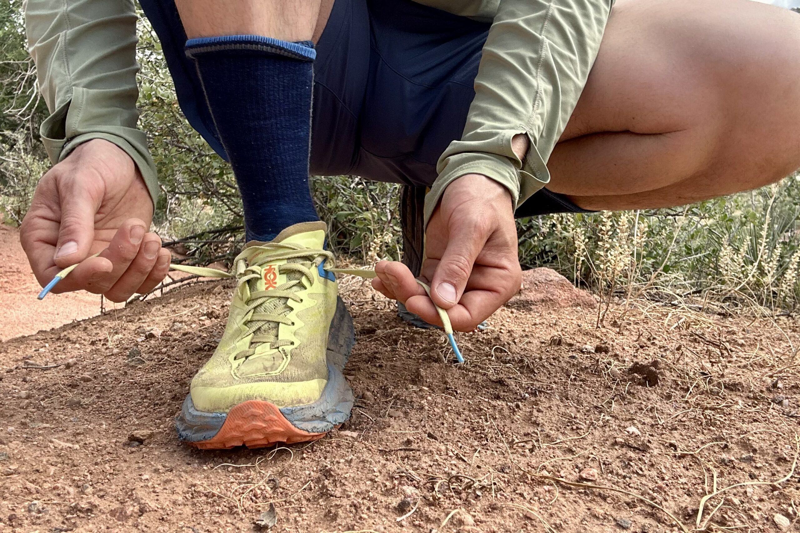 Shot of a hiker from the knees down crouching to tie his trail running shoes.