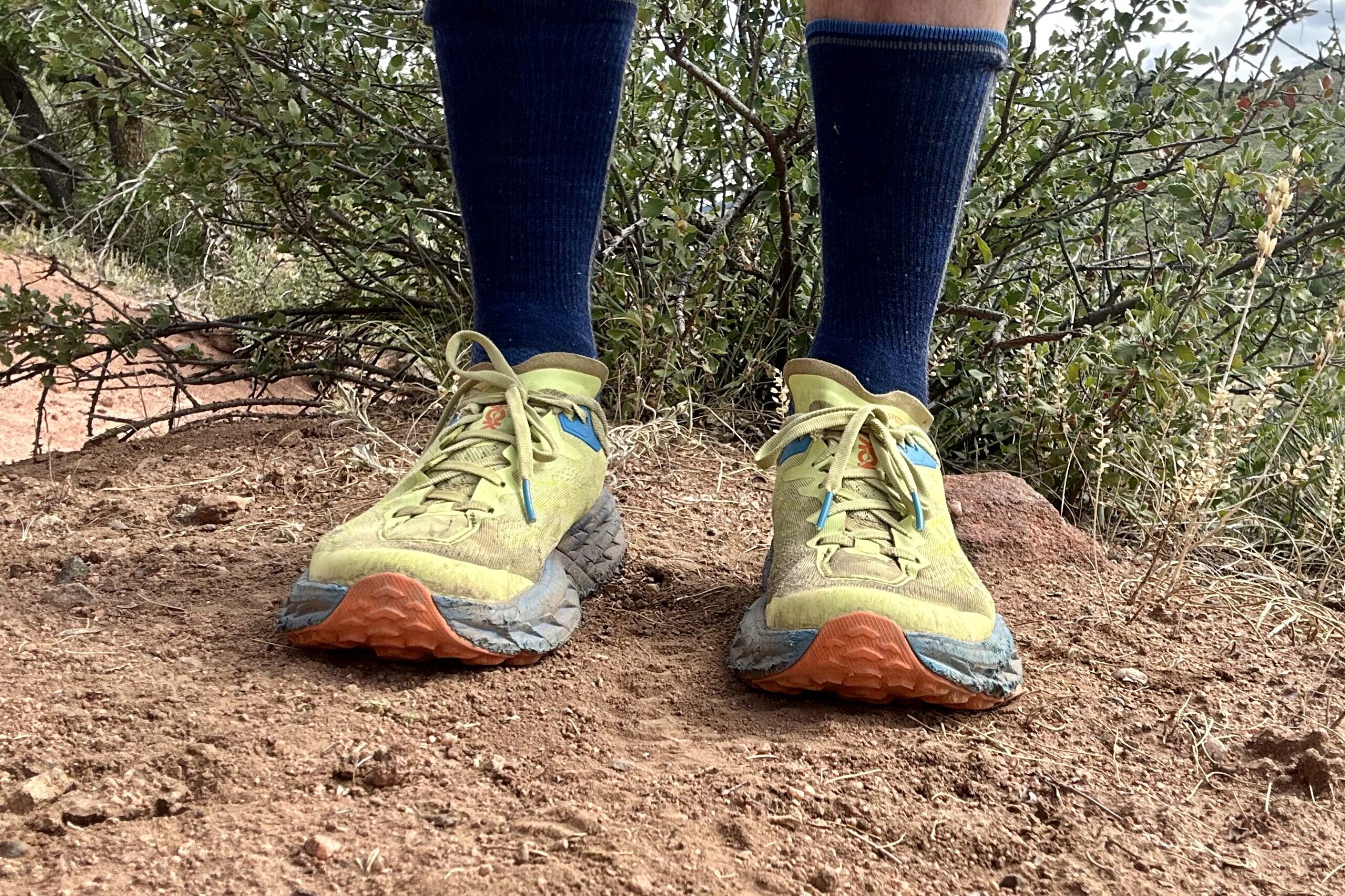 Closeup of trail running shoes from the knees down in a desert setting, straight on.