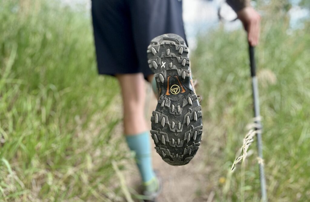 A hiker shows off the traction of his right shoe, which is in focus, and the rest of the shot is blurred.