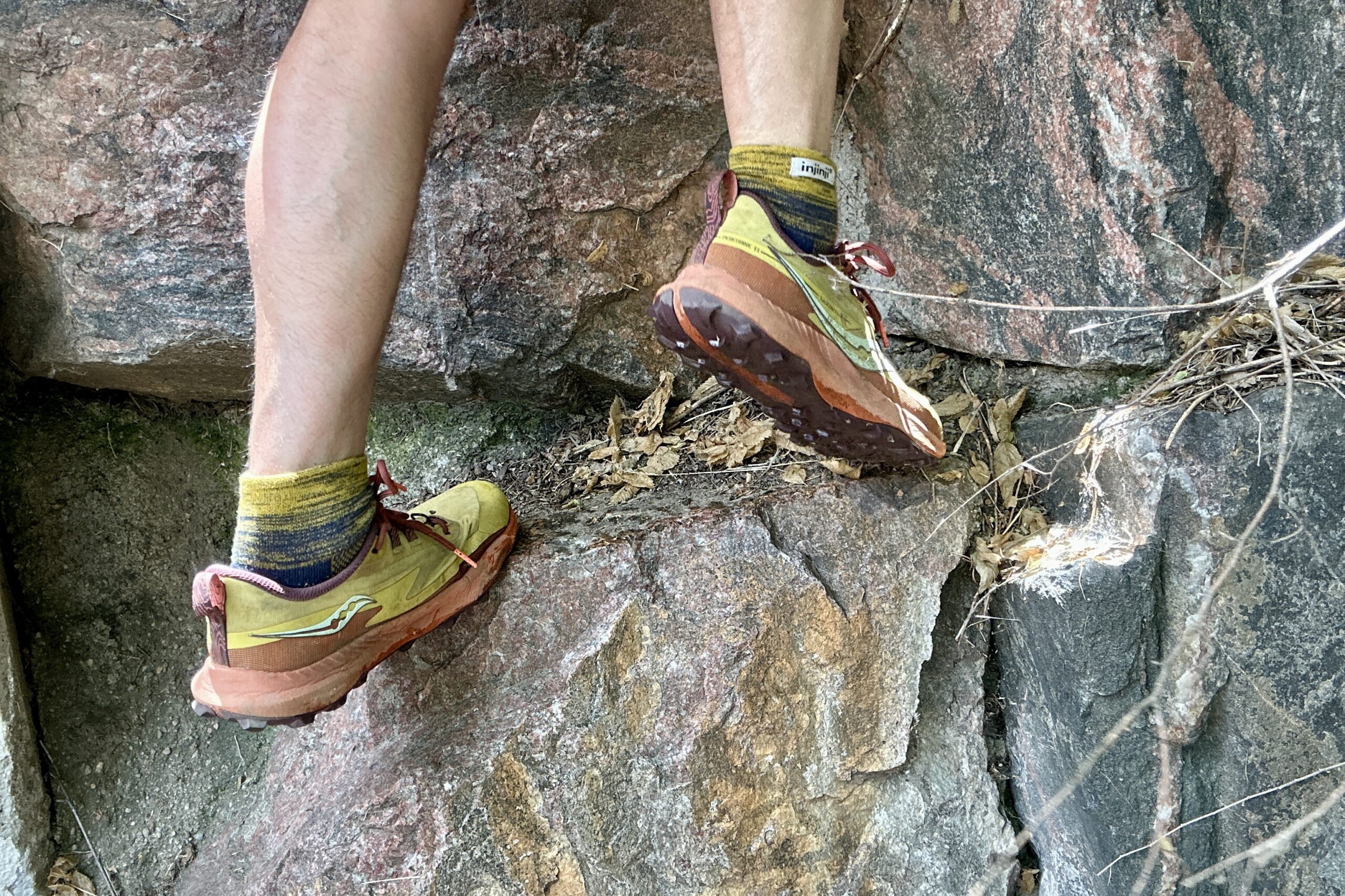 Man's legs from knee down wearing yellow and black socks with Saucony Peregrine 14 running shoes climbs some rocks.