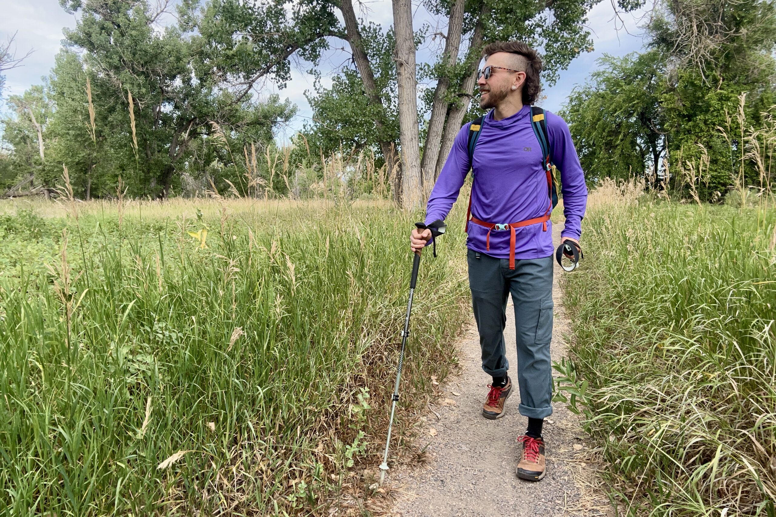 A man in a purple sun shirt hikes in a wilderness area looking off in the distance.