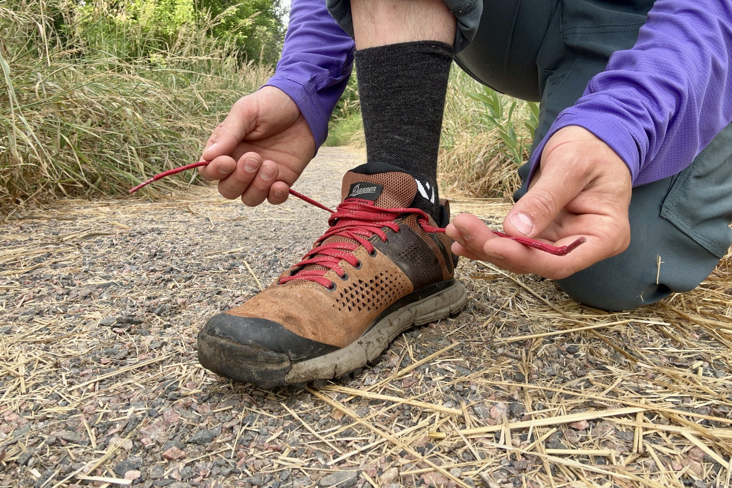 A close up shot of a man tying the red laces of a pair of Danner Trail 2650 hiking shoes.