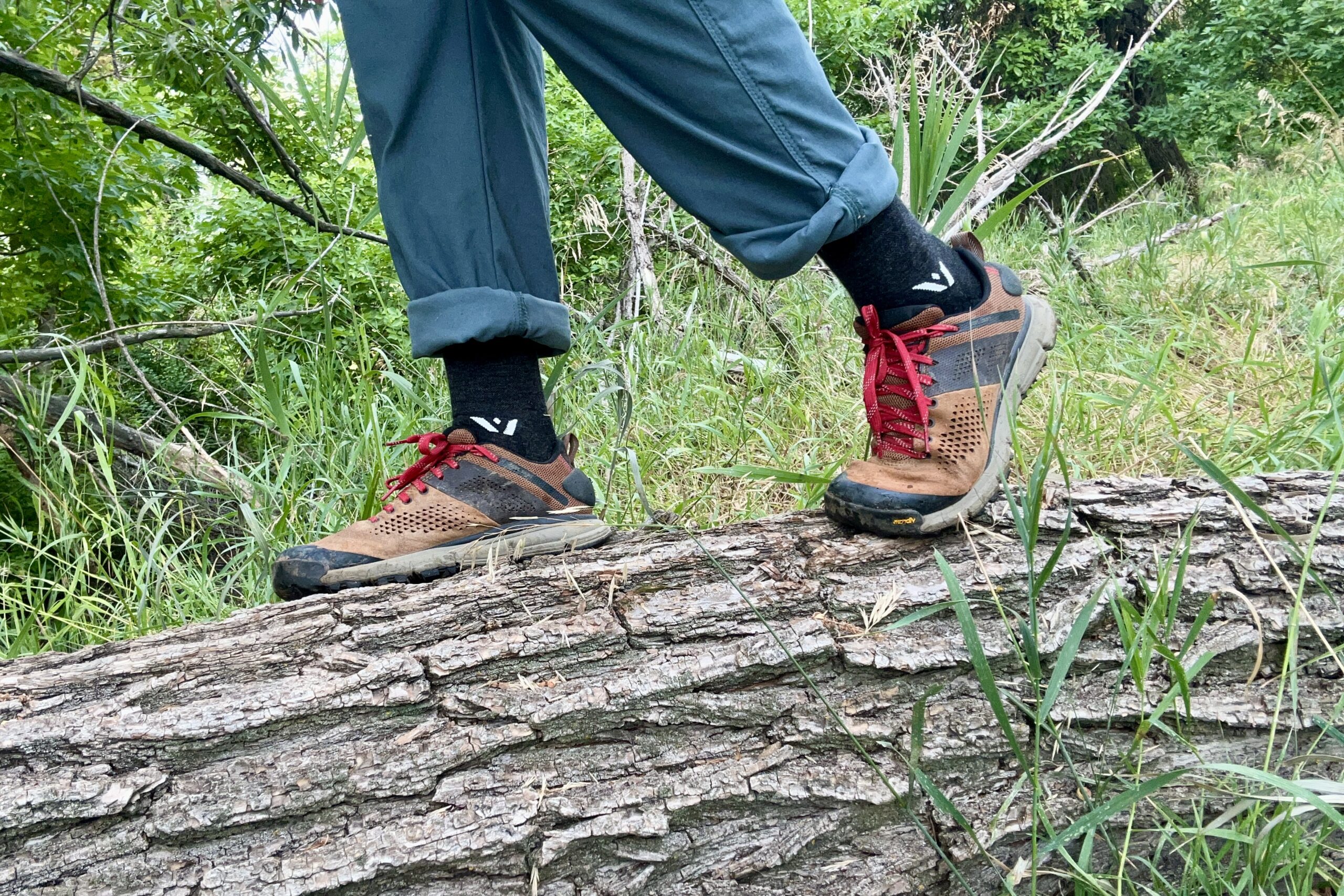 A close up shot from the knees down of a man wearing the Danner Trail 2650 hiking shoes while standing on a log.