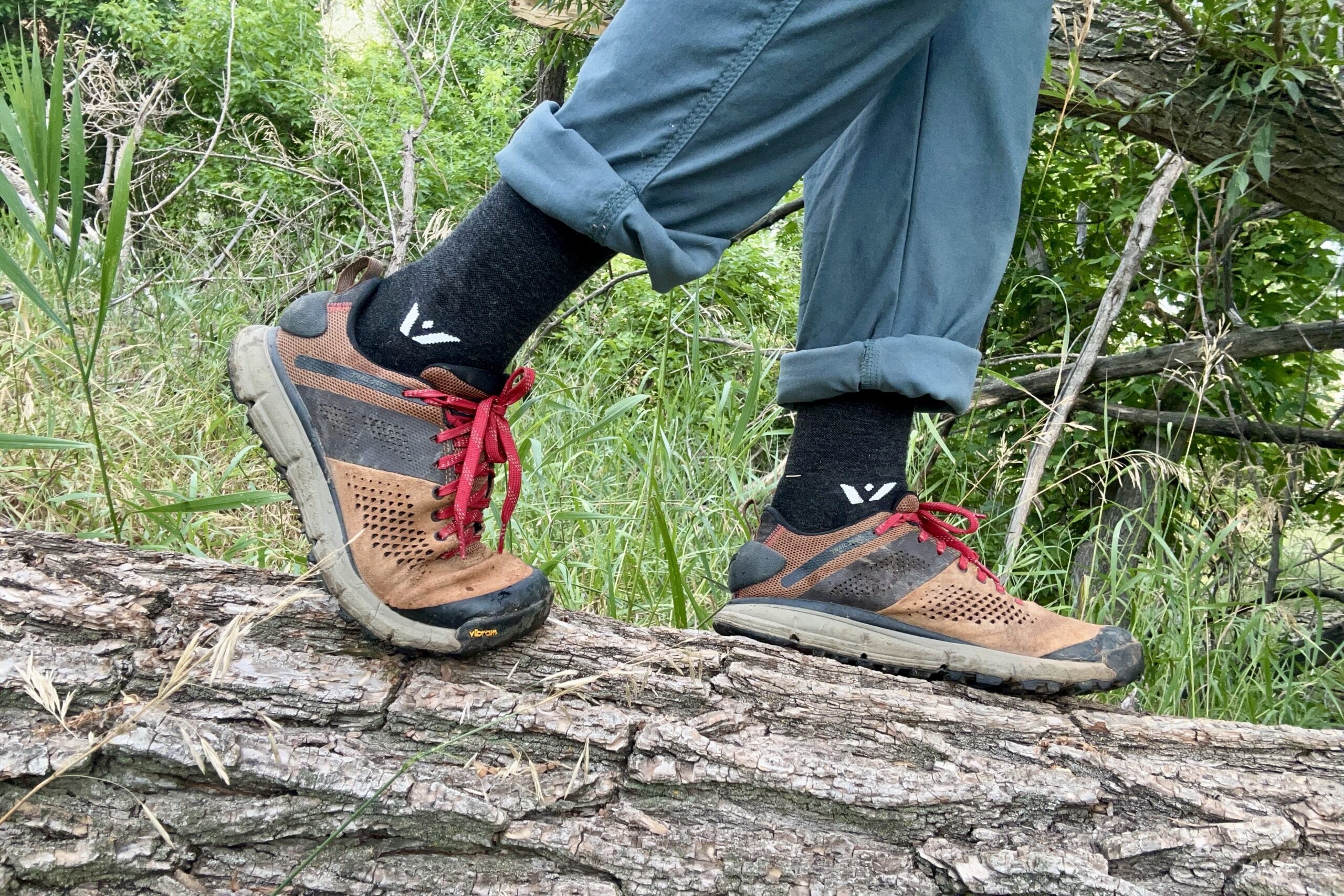 A close up shot from the knees down of a man wearing the Danner Trail 2650 hiking shoes while standing on a log.