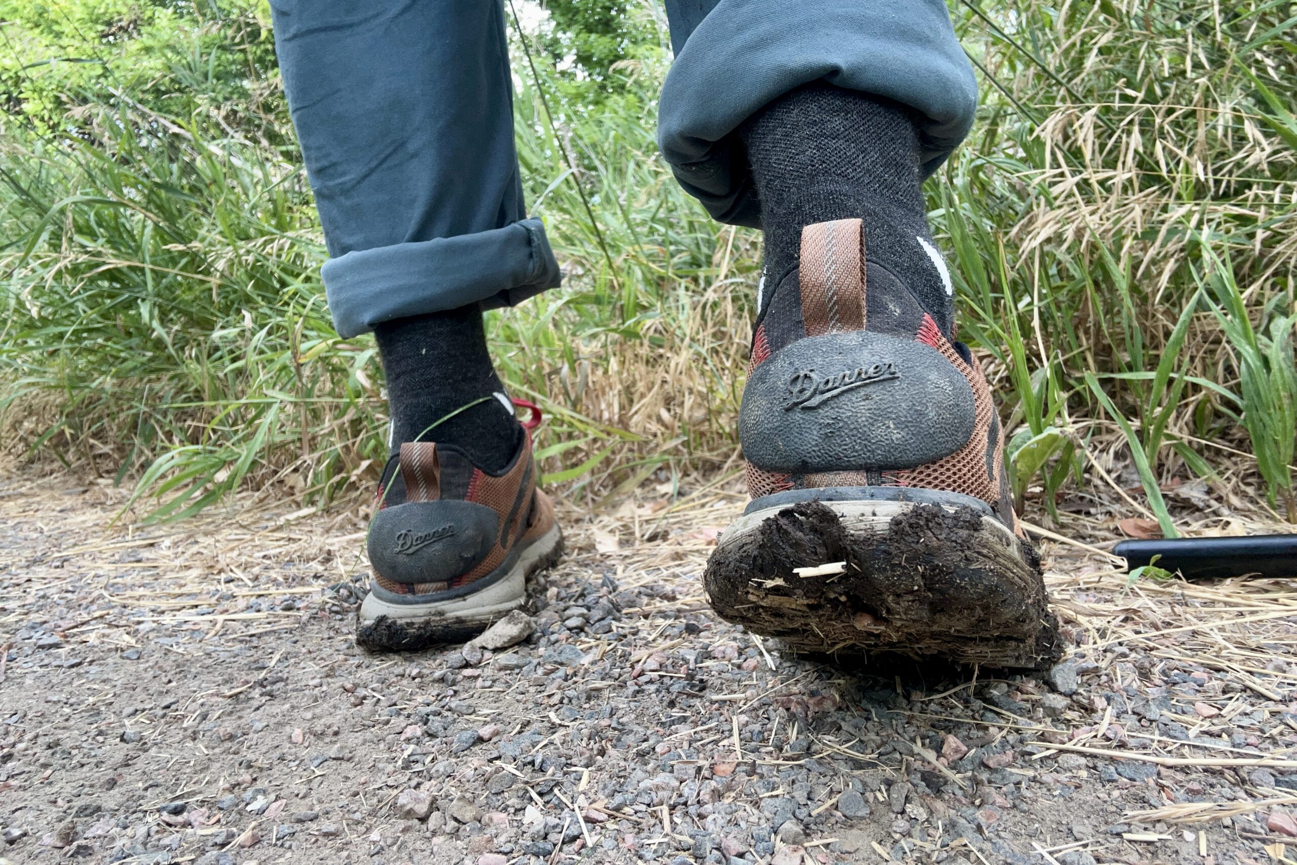 A close up shot from the knees down of a man wearing the Danner Trail 2650 hiking shoes from behind to show off the giant rubber heel caps after hiking through mud.