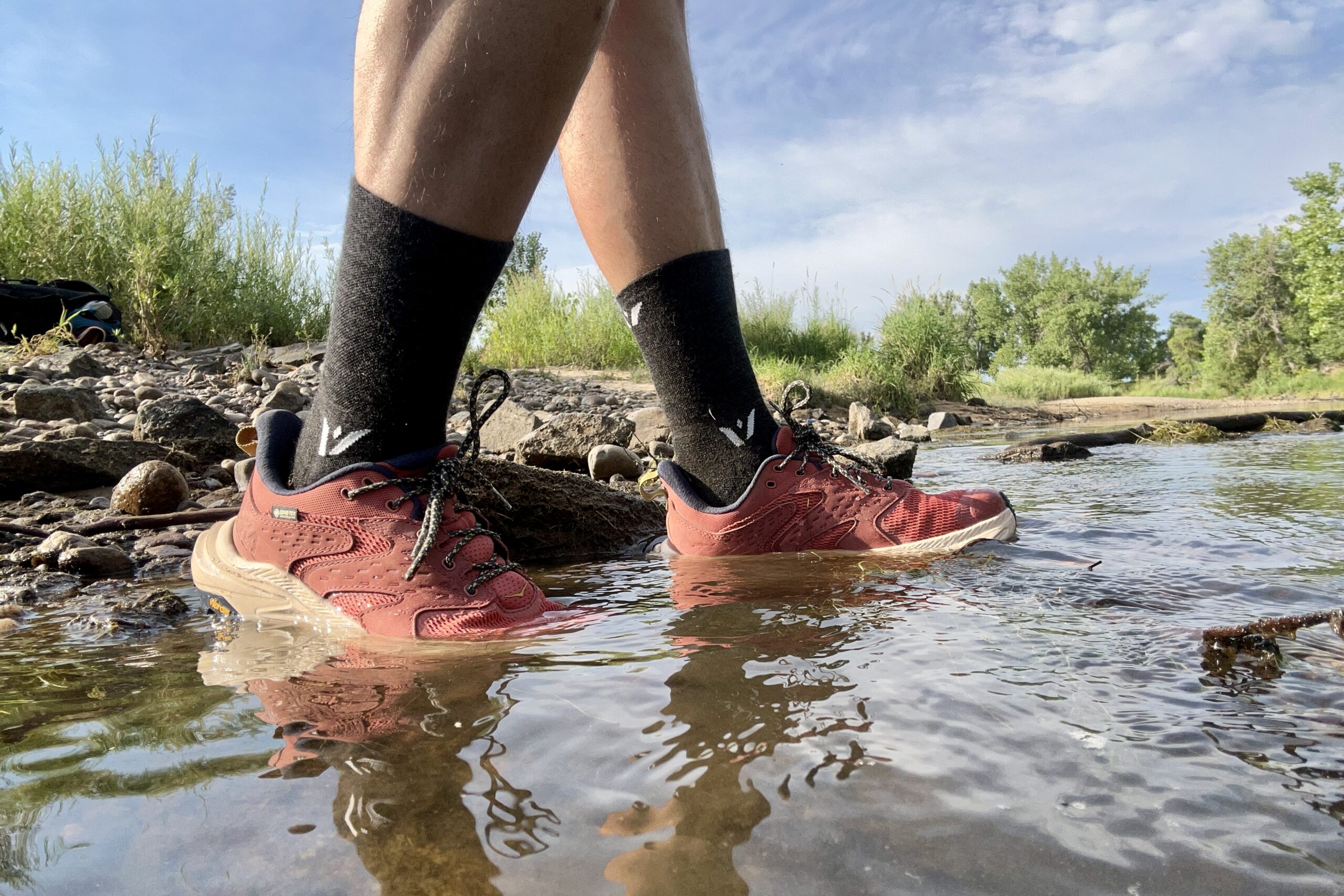 A close up of a man wearing the HOKA Anacapa 2 hiking shoes in several inches of water.