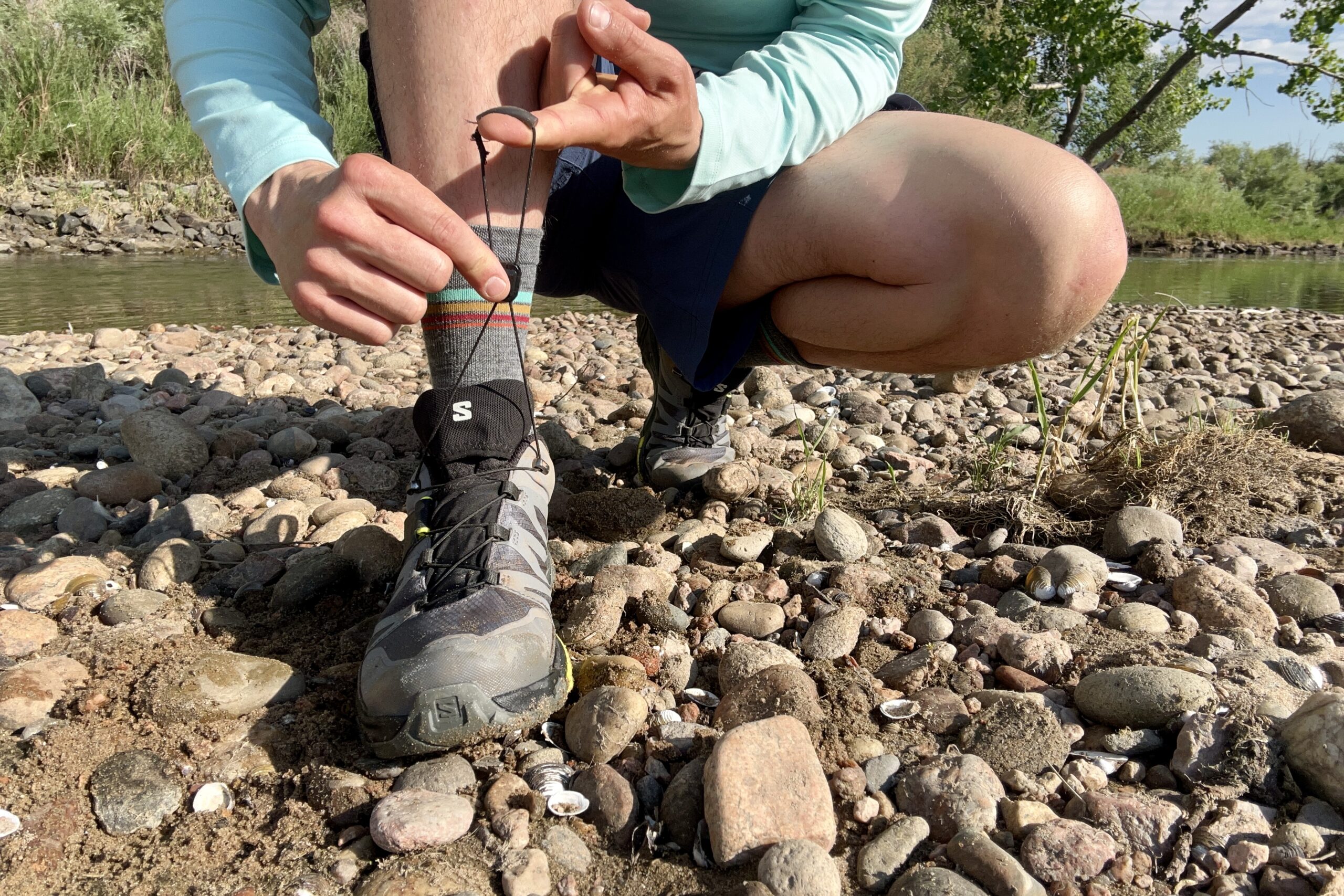 A close up shot of a man tying the Quicklace system on the Salomon Ultra GTX 4 shoes in mud and water.