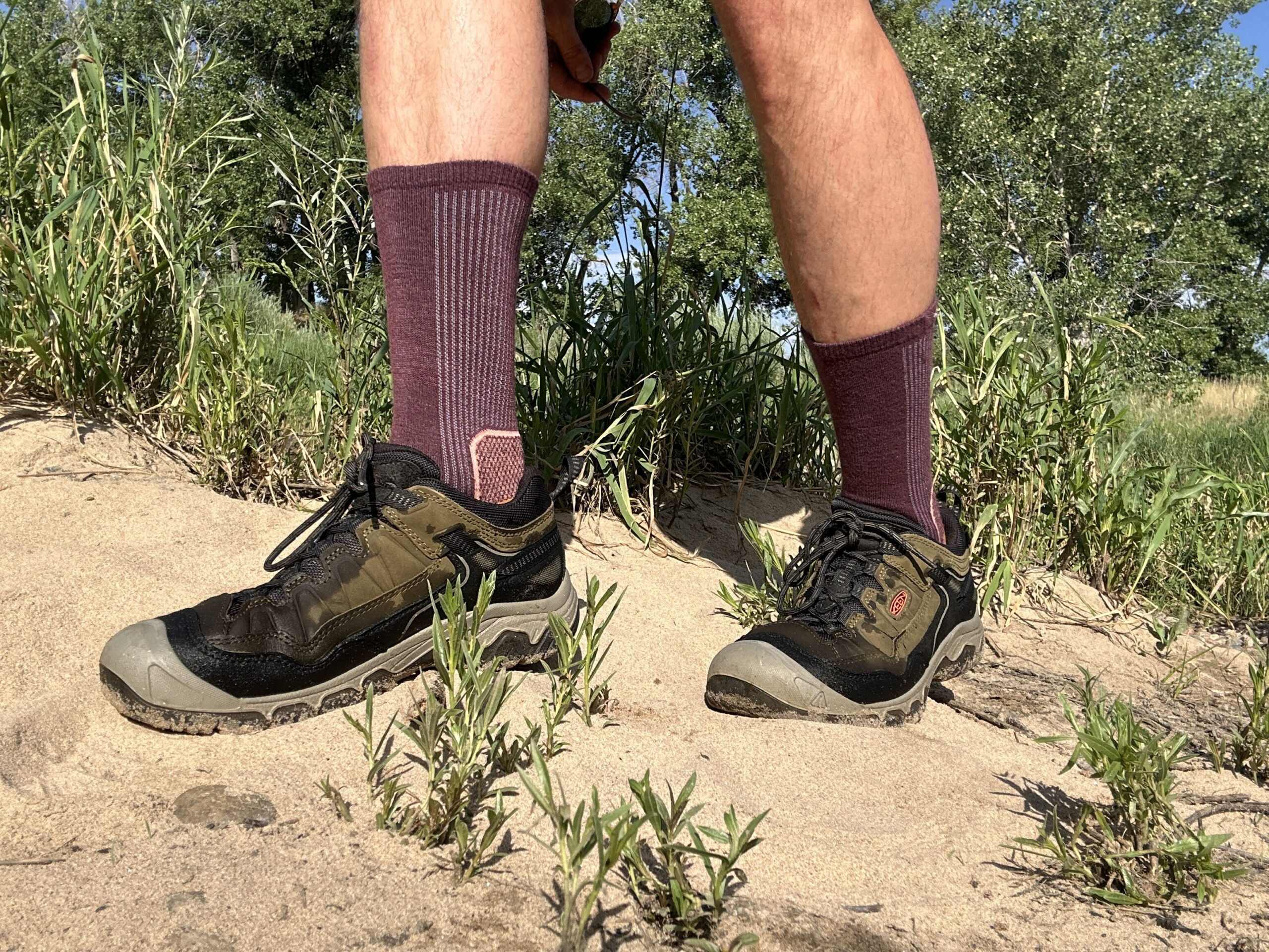 A close up view of the Keen Targhee IV hiking shoes from the side on sandy terrain, showing off their profile and design.