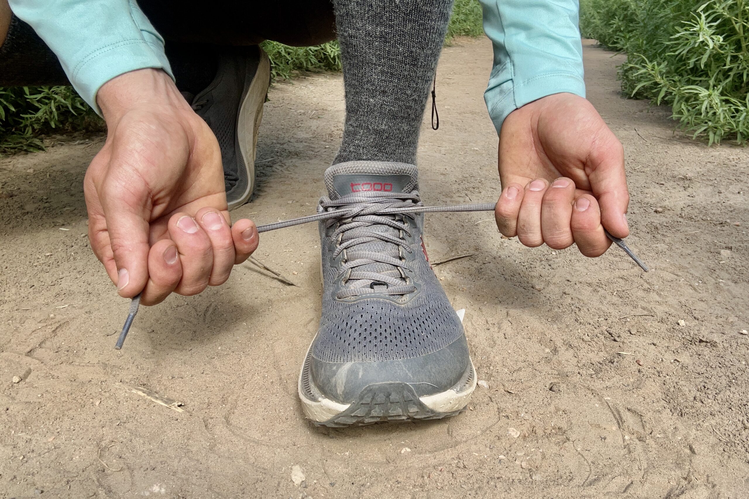 A close up shot of a man tying the shoelaces of a pair of men's Topo Athletic Ultraventure 3 shoes.