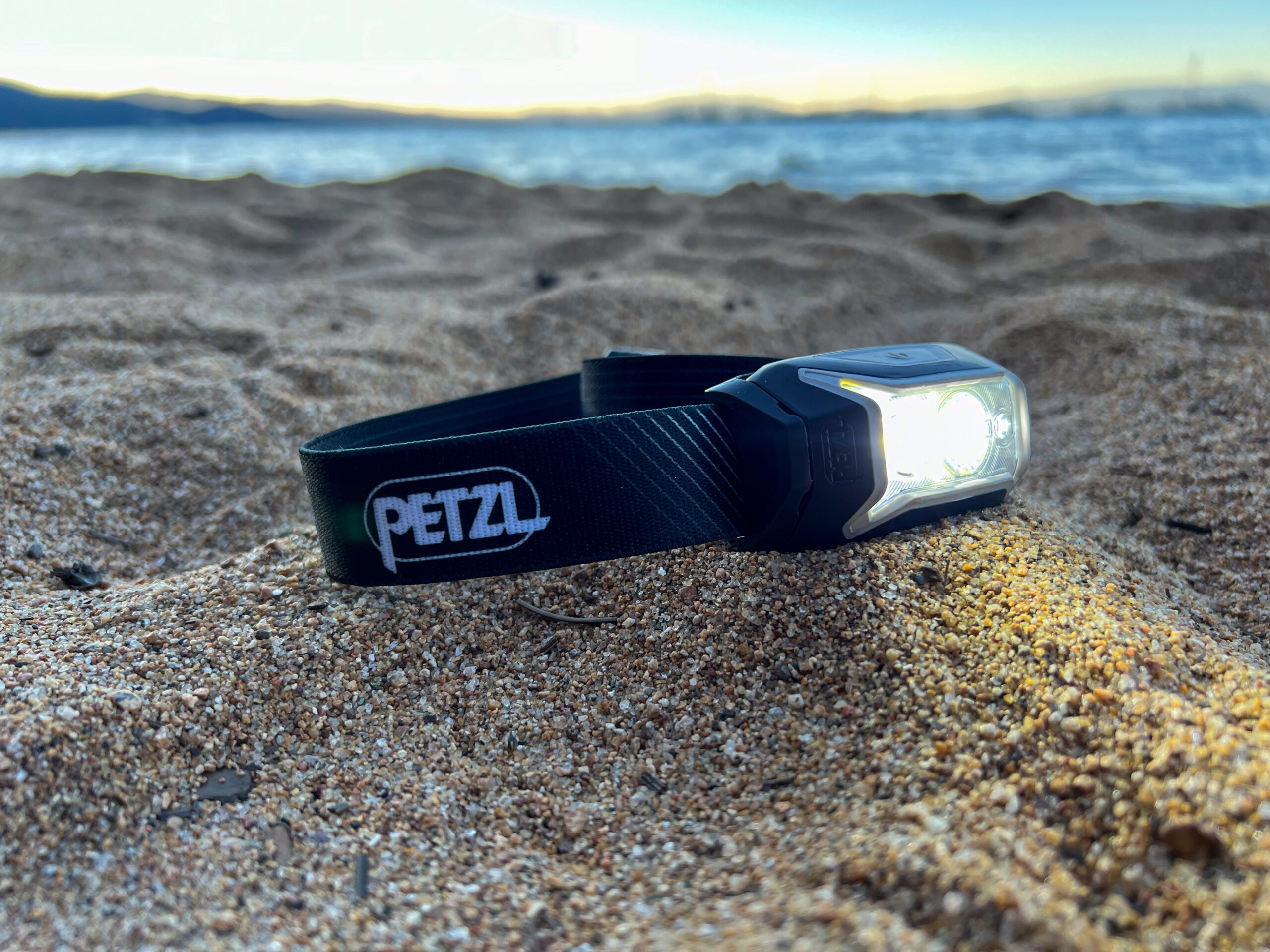 The image shows a headlamp laying in the sand at sunset.