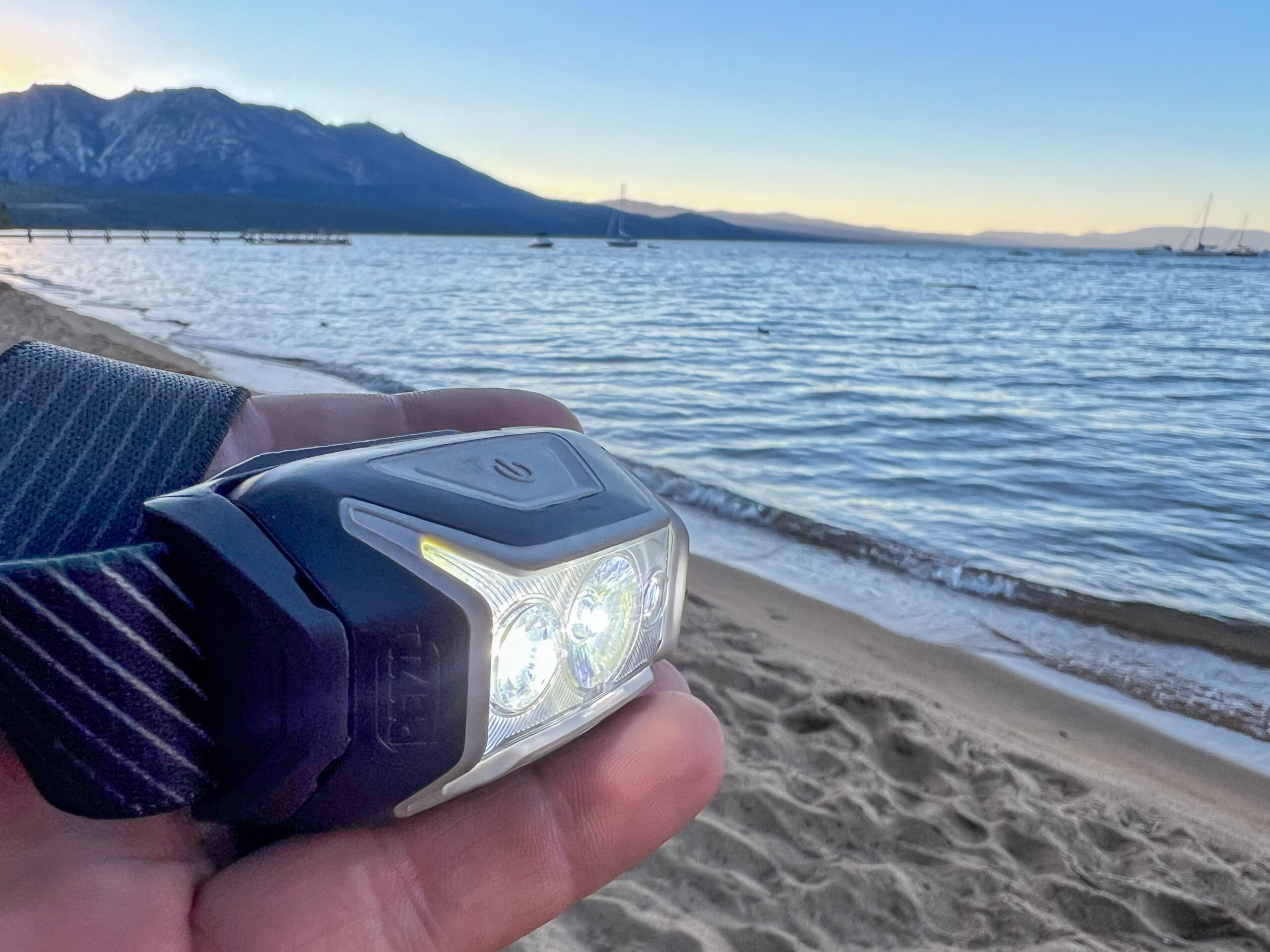 The image hows the Petzl Actic CORE in the hand of a camper with a lake in the background.