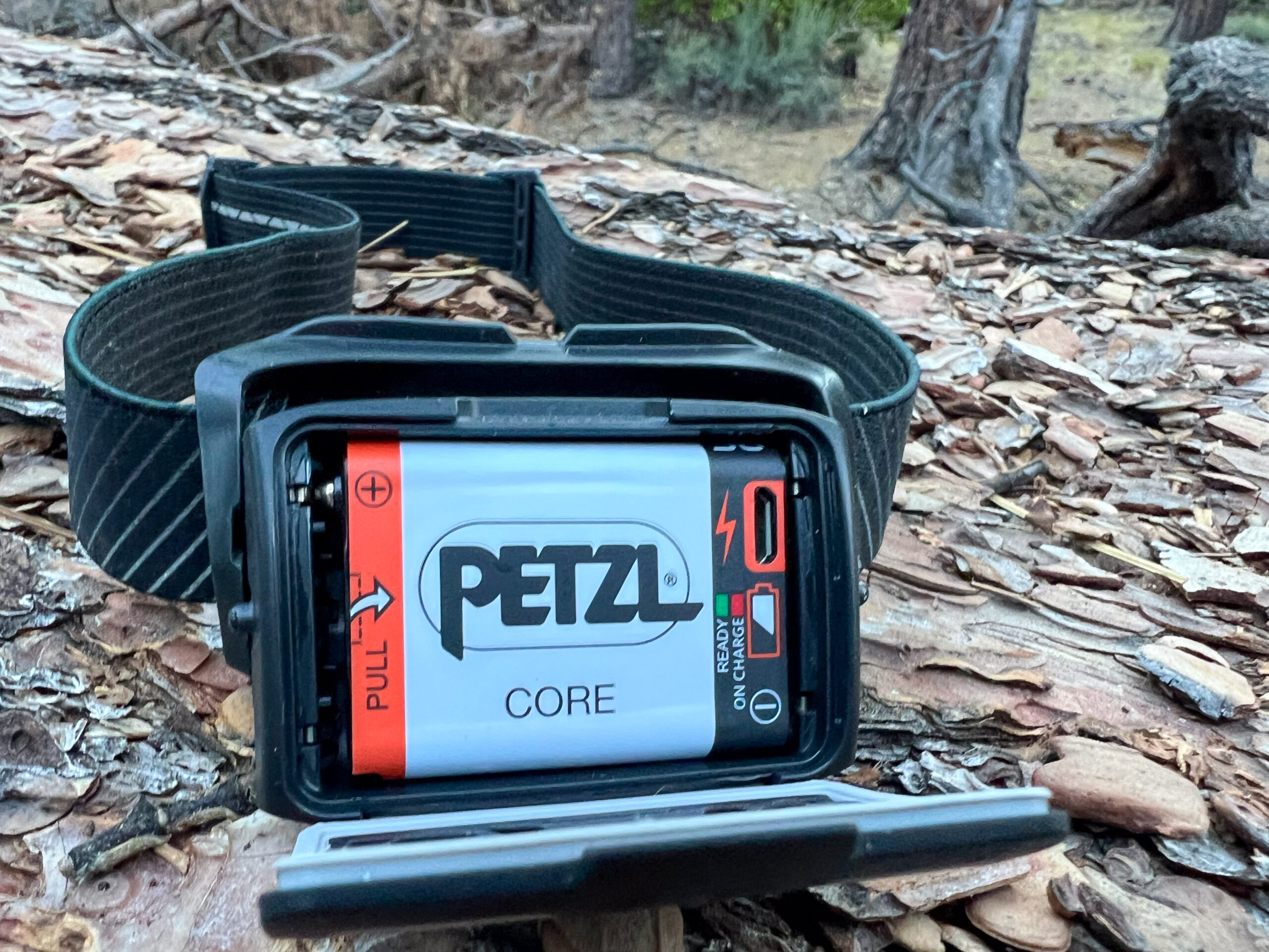 The image shows the Petzl Actik CORE headlamp from the rear. The battery compartment is open exposing the rechargeable battery pack.