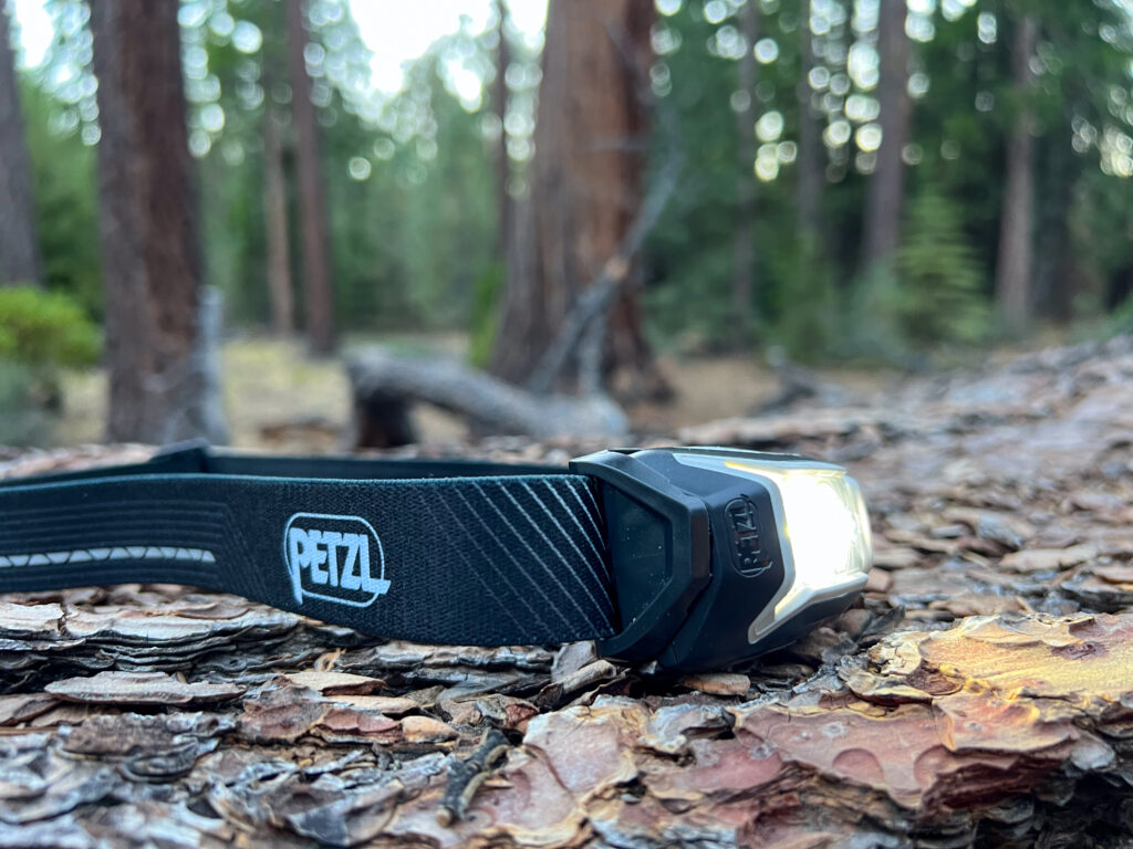 The image shows the Petzl Actik Core headlamp laying on a log in the forest.