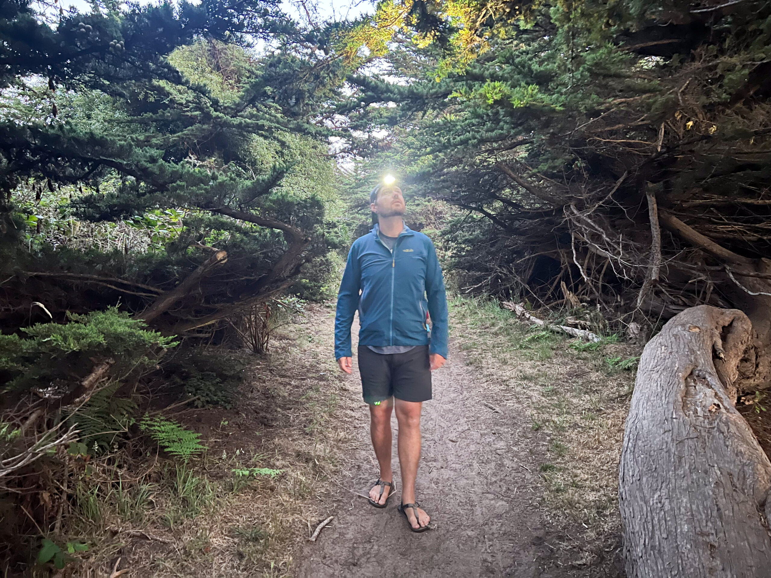 The image shows a man walking in the woods with a headlamp.