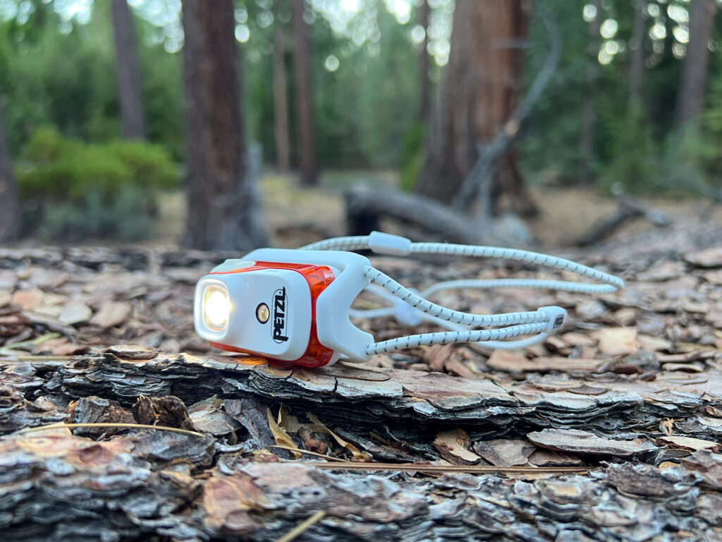 The image shows a side view of the Petzl Bindi headlamp sitting on the forest floor.