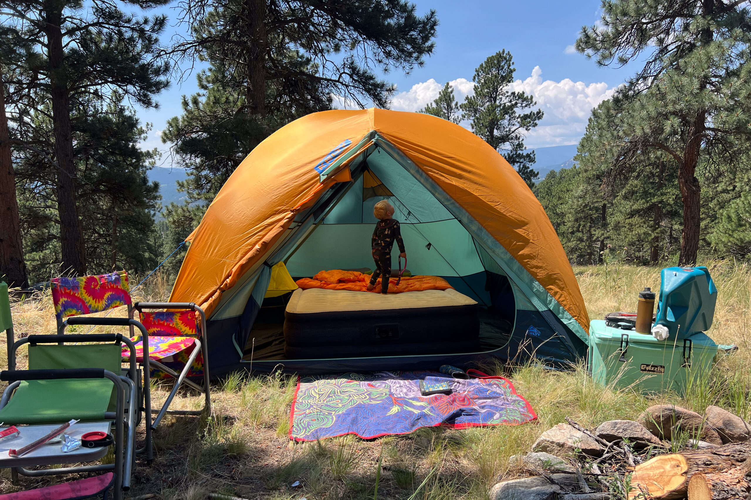 The image shows a medium show of the Wireless 6. Inside there is a queen sized air mattress and a child playing in the tent. The tent is in a grassy environment and it's surrounded by pine trees.