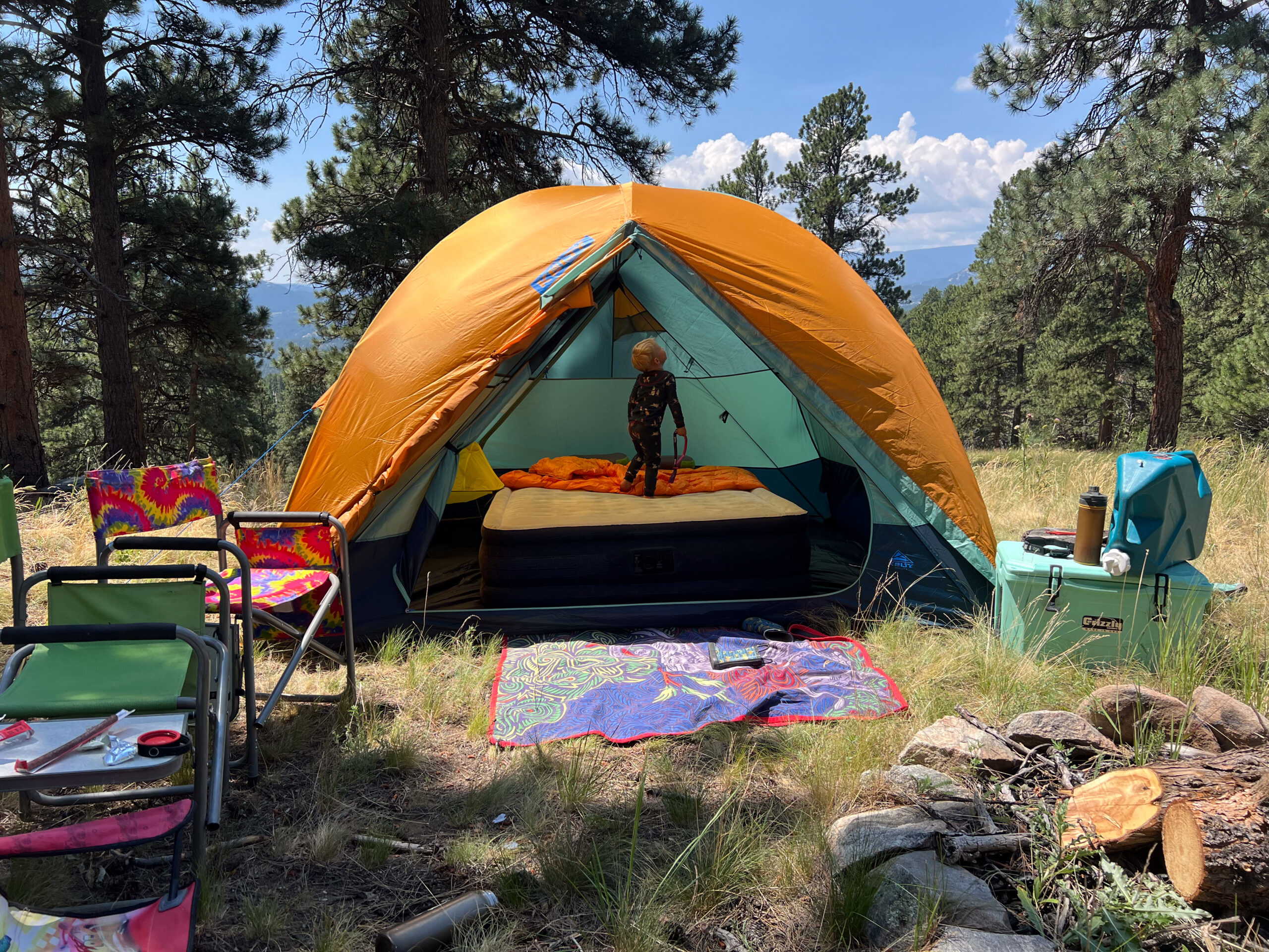 The image shows a medium show of the Wireless 6. Inside there is a queen sized air mattress and a child playing in the tent. The tent is in a grassy environment and it's surrounded by pine trees.