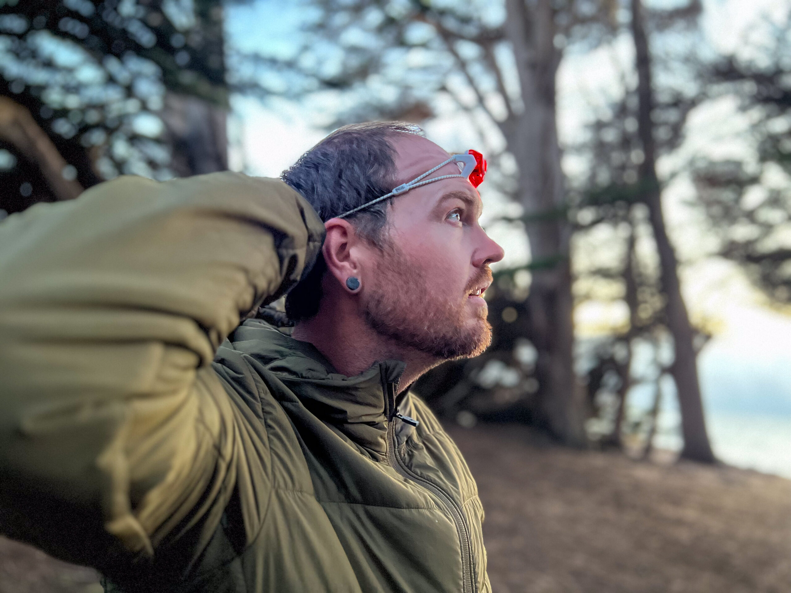 The image shows a hiker adjusting his headlamp in a forest setting.