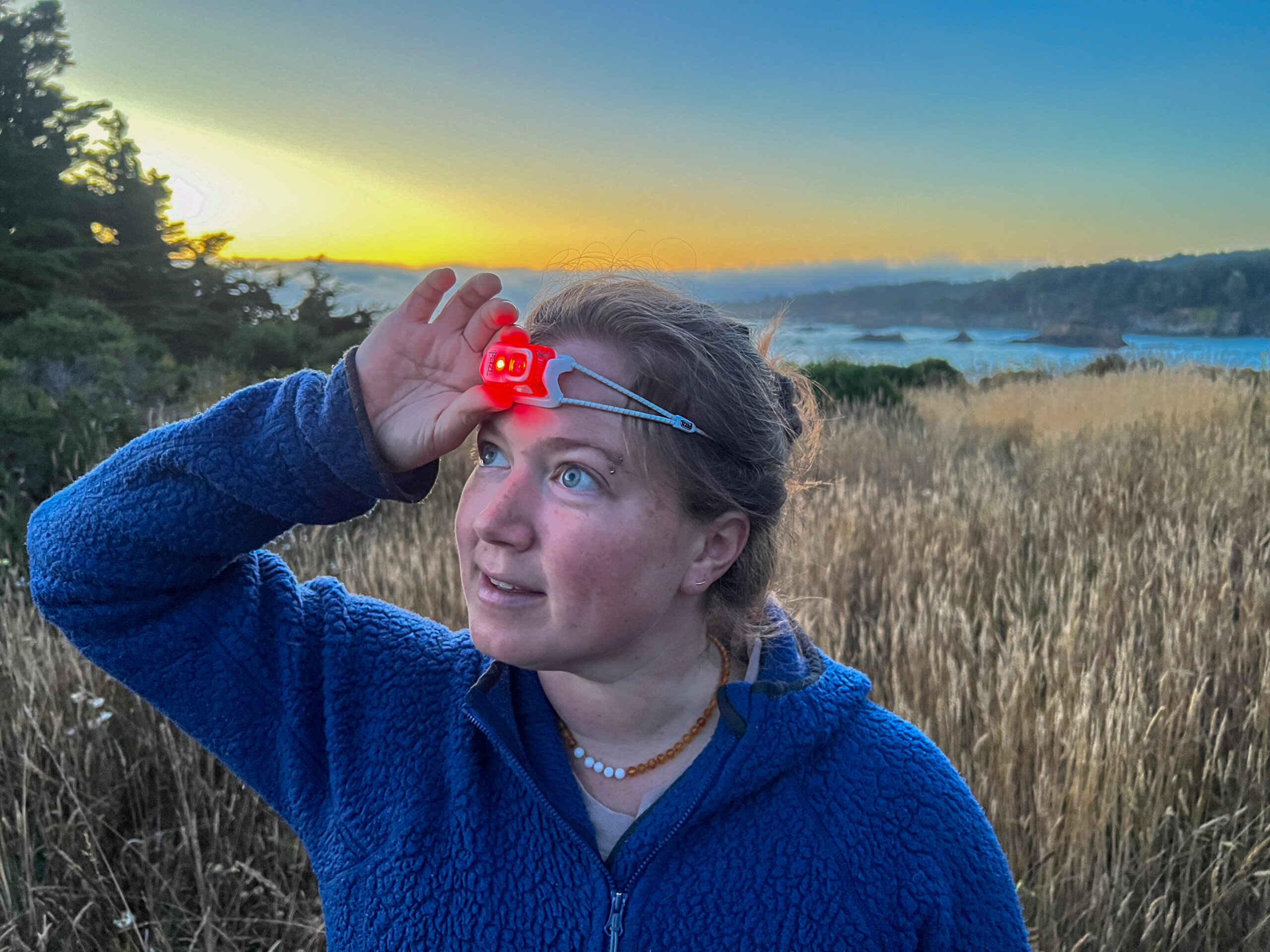 The image shows a smiling hiker looking at the camera while wearing a headlamp with it's red light feature activated.