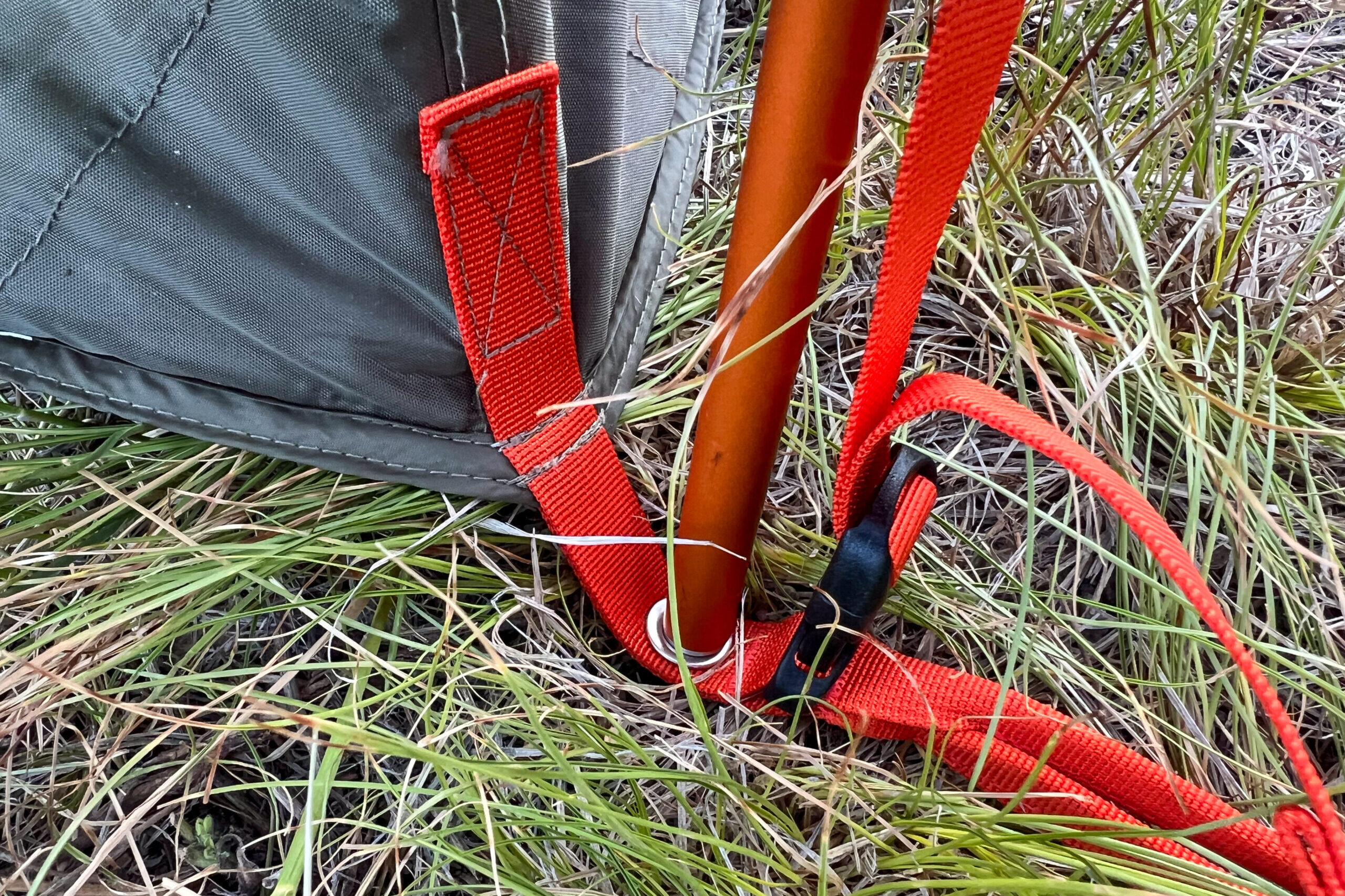 The image shows the color coded hardware that makes the REI Wonderland 4 easier to setup. The image shows an orange pole through the orange grommet webbing in the corner of the tent.