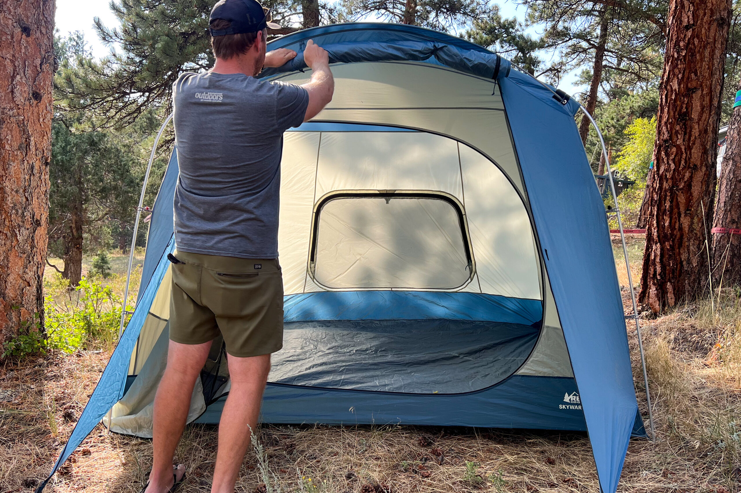 The image shows a male hiker rolling up the center section of the front vestibule on the REI Skyward 4.