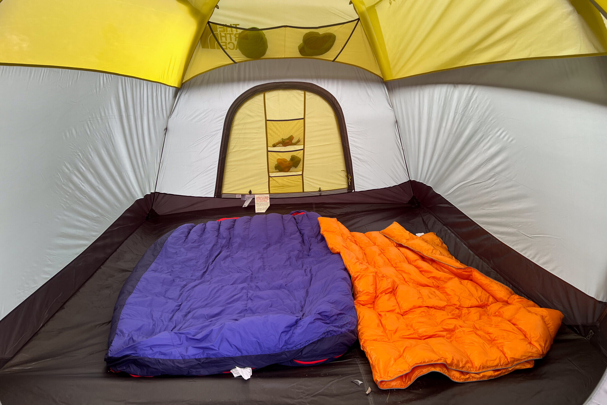 The image shows the interior of The North Face Wawona 6 tent. There are two sleeping bags in the tent and gear in the mesh pockets against the rear wall.