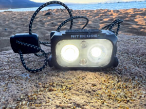 The image shows a black Nitecore NU25 UL sitting on the beach.