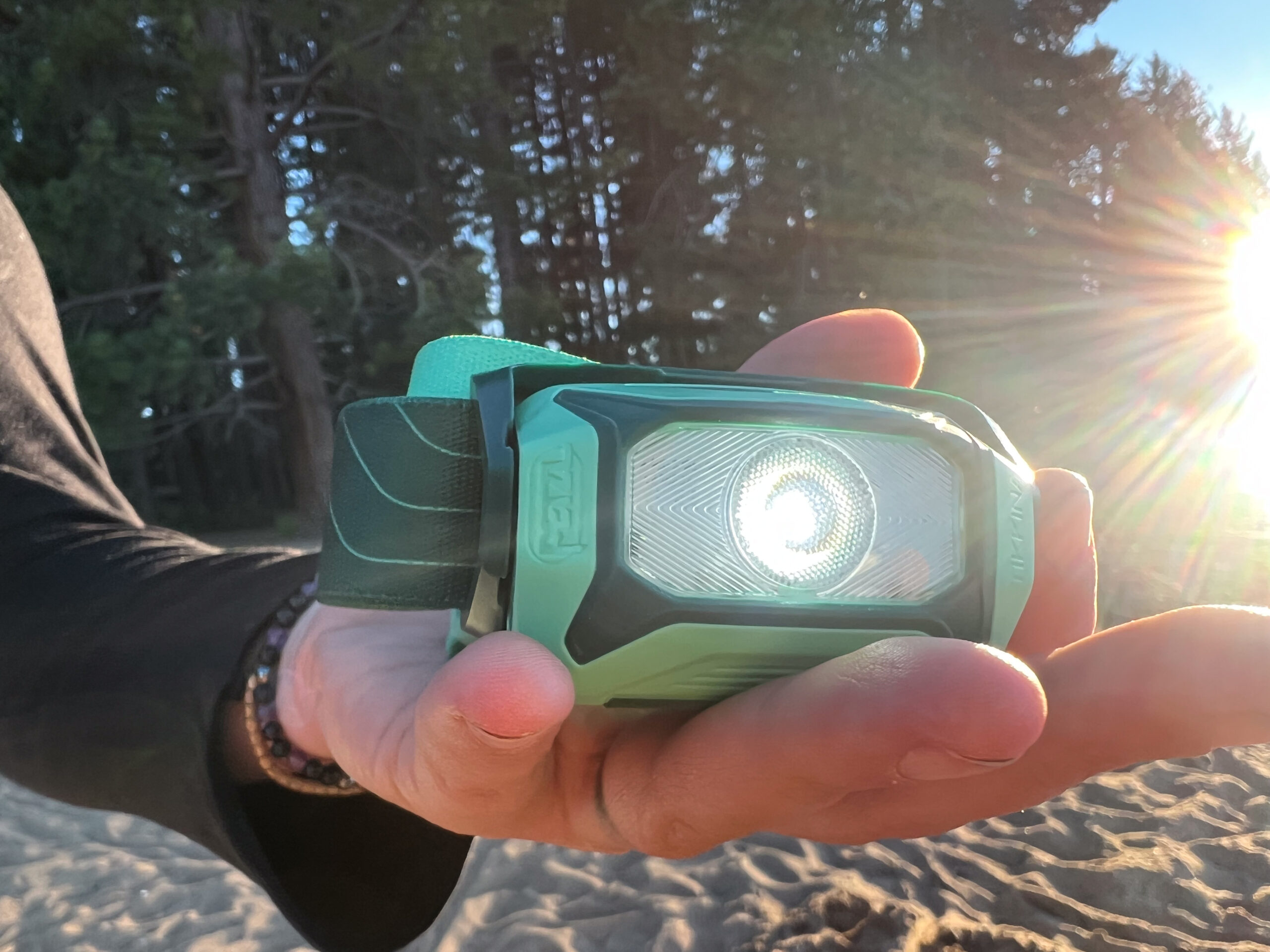 The image shows a headlamp in the palm of a camper on the beach