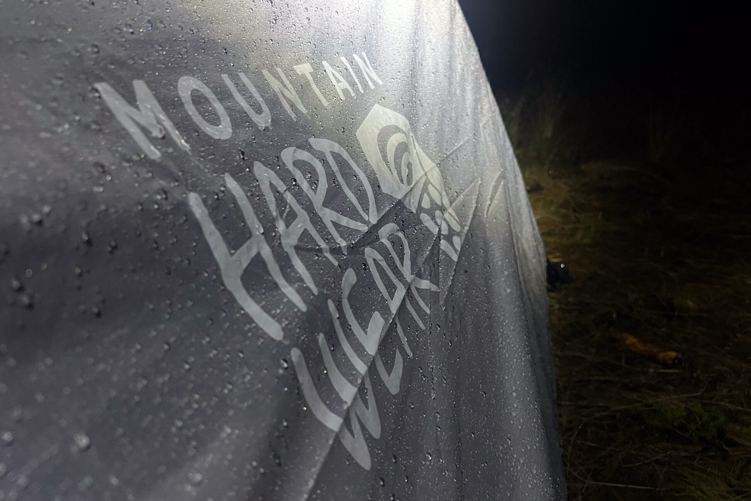 The image shows the wet rainfly of the Mountain Hardware Mineral King 3 illuminated by a headlamp at night. The background is dark.